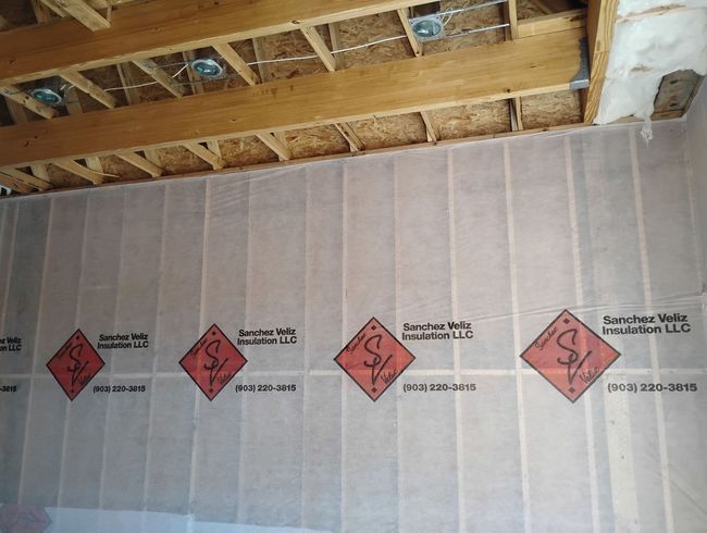 Worker installing pink insulation in a wall cavity with a power drill
