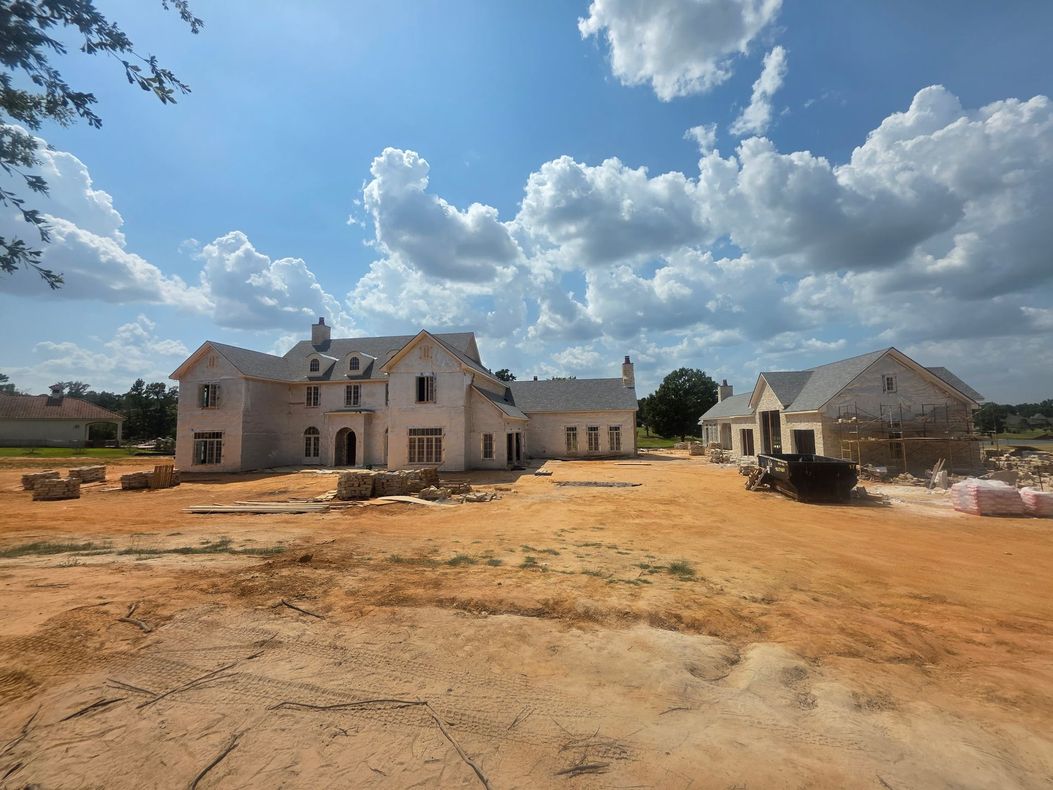 Partially built houses on a dusty lot under a bright blue sky with clouds
