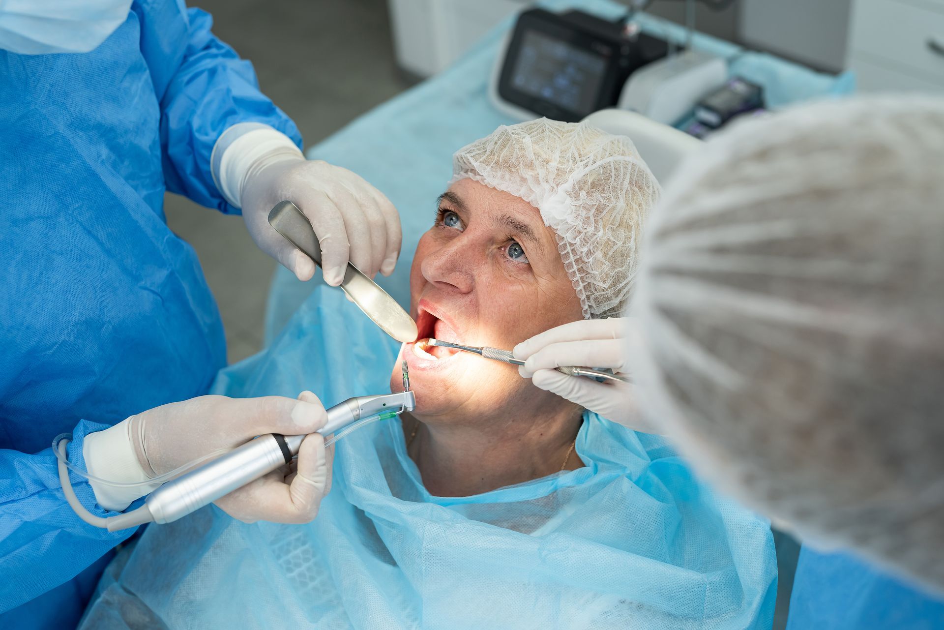 Dentists operating on a patient's open mouth in a medical setting.