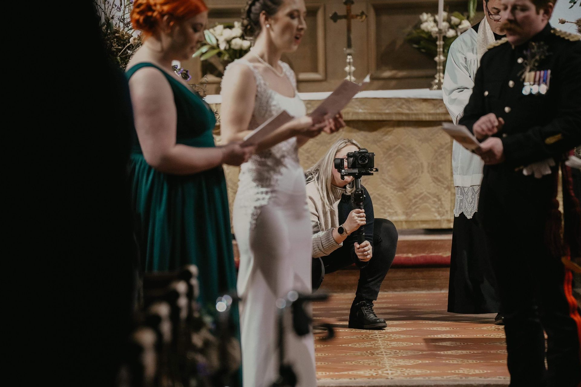 Bride reading vows at altar during wedding ceremony, with photographer kneeling in the aisle