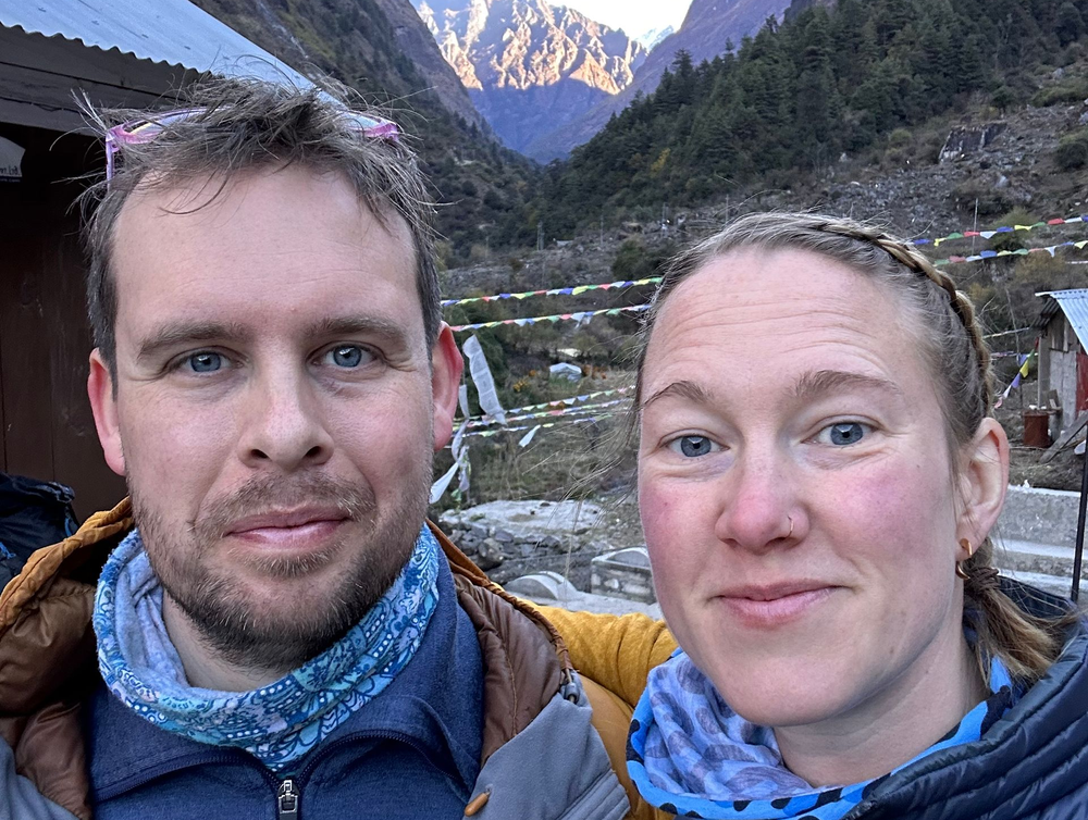 Chris & Sophie Lambert taking a selfie outdoors with mountains and prayer flags in the background