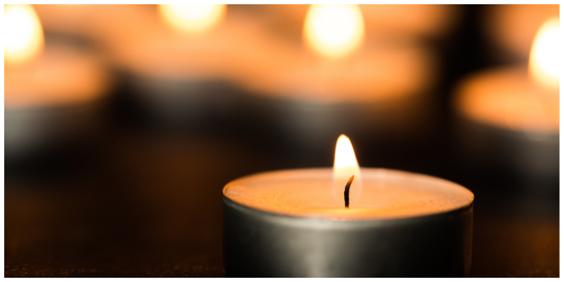 Lit candle in a metal holder with warm blurred lights in the background