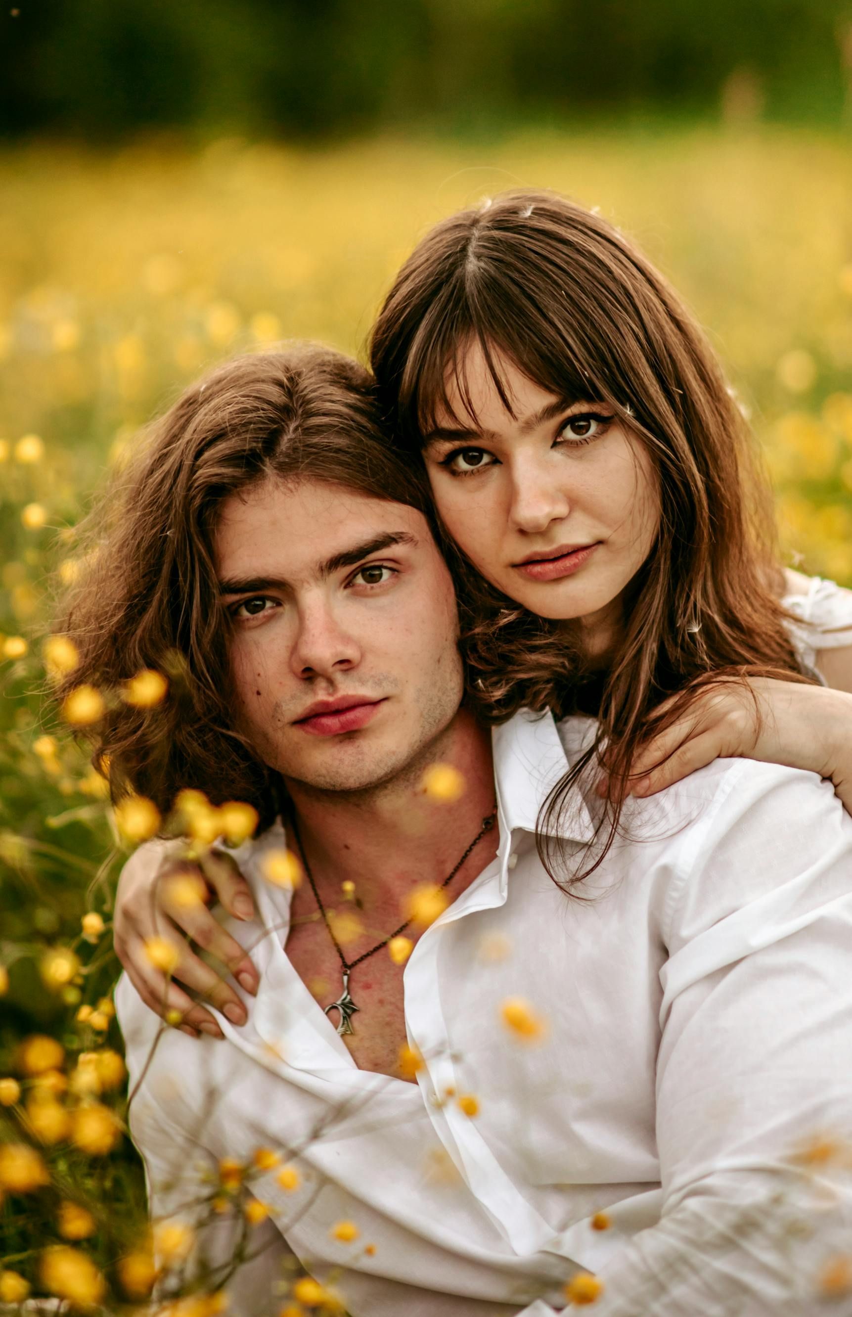 Two people in a field, with one in a white shirt holding the other amid yellow flowers.