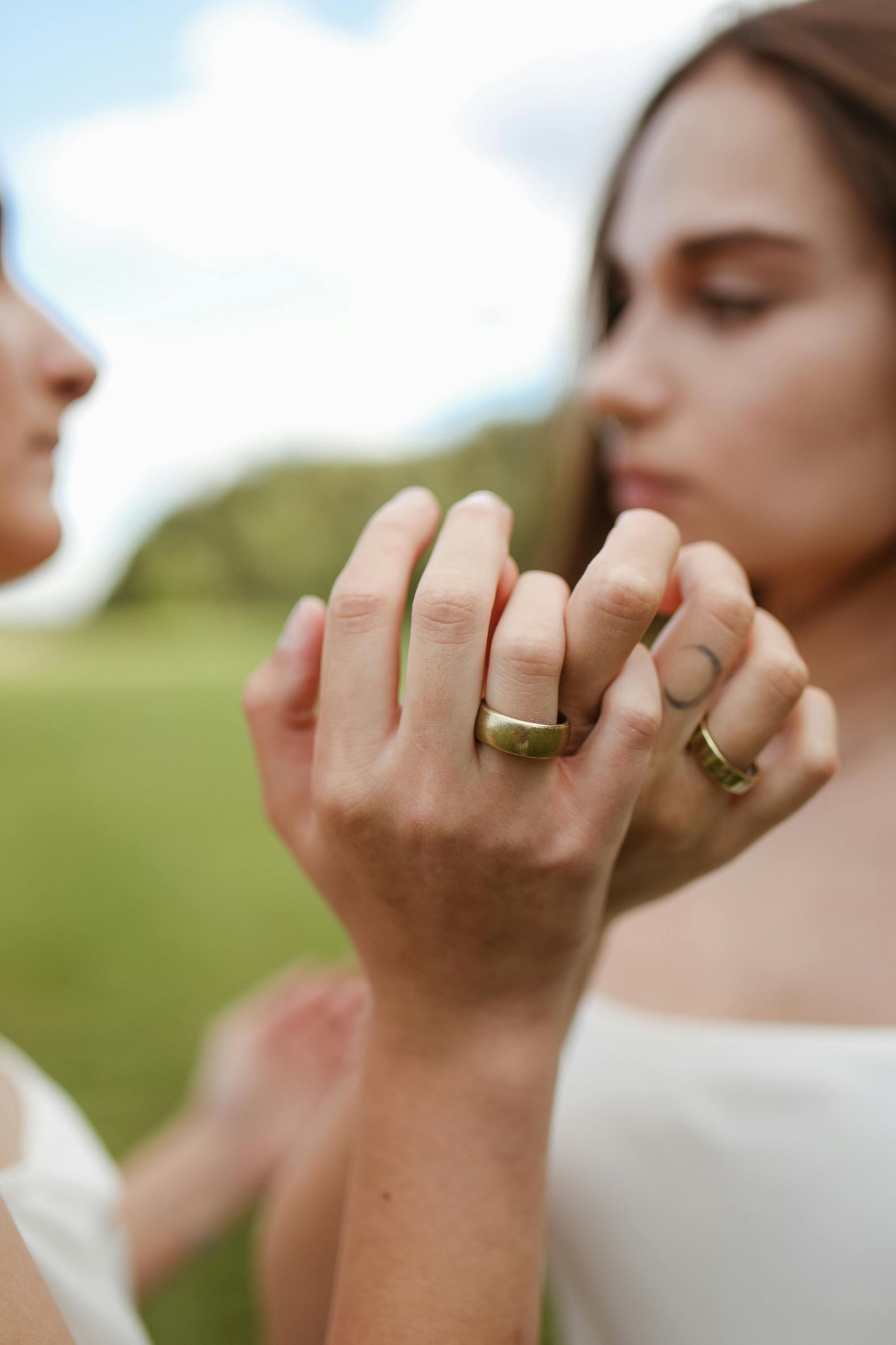 Close-up of two people holding hands outdoors, with gold rings visible, against a blurred green background