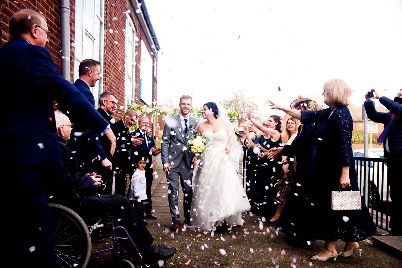 Wedding in the lake district exiting a brick building through falling confetti, guests cheering on both sides