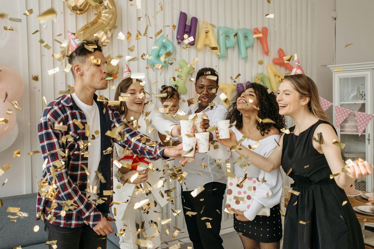 Friends toasting with drinks amid confetti at a colorful birthday party