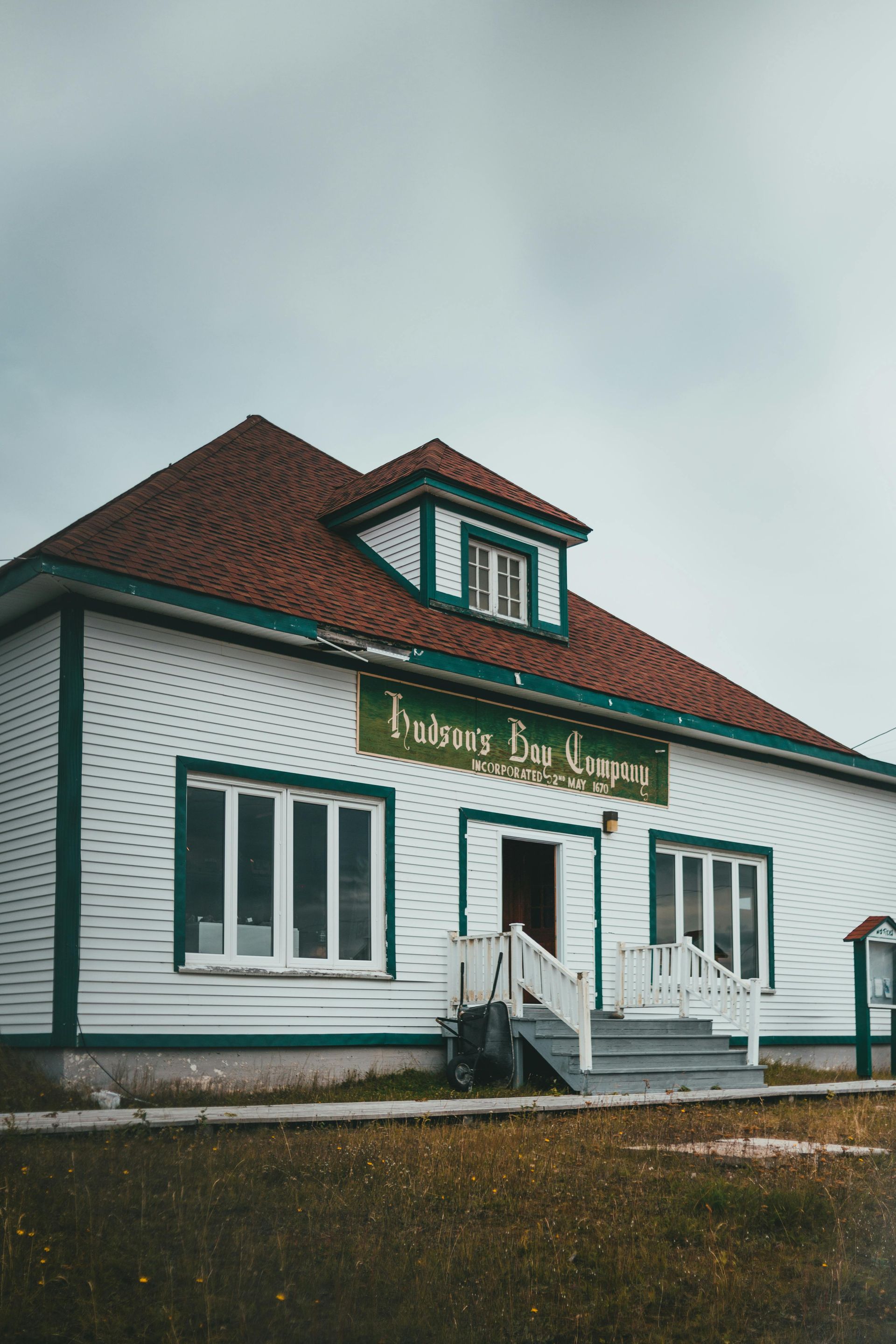 White building with green trim and red roof, a sign above the entrance, under an overcast sky