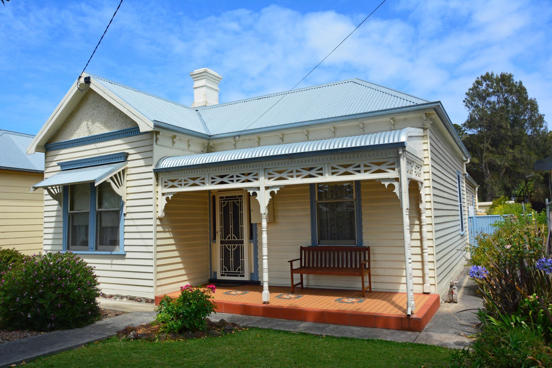 White cottage with a blue roof and front porch, sitting in a grassy yard.