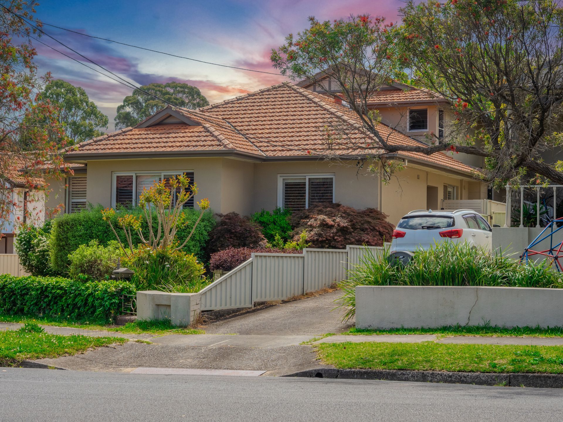 Suburban house with tiled roof, front garden, driveway, and parked car at dusk