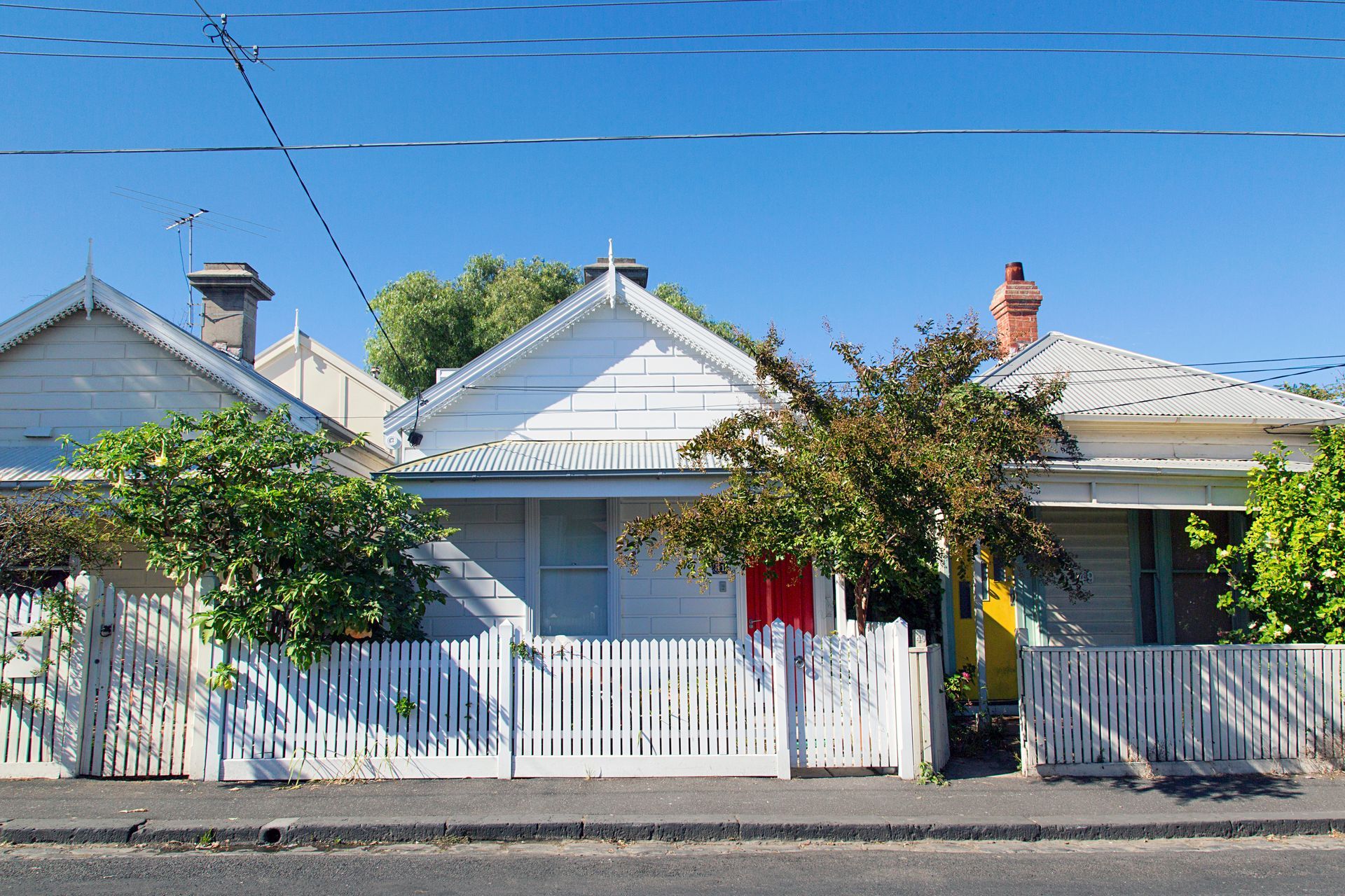 Row of white cottages with picket fences and trees under a clear blue sky