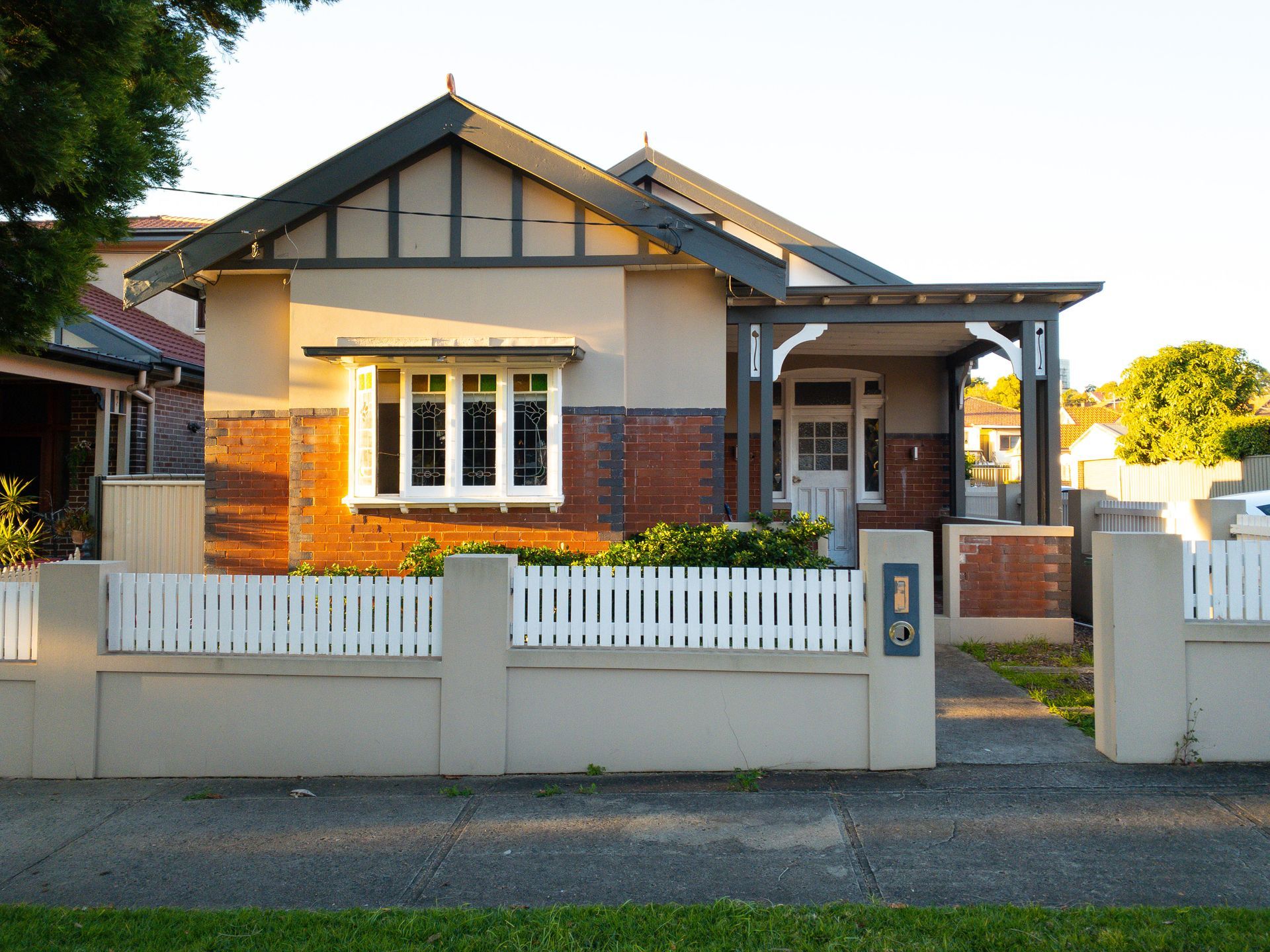 Single-story brick house with white picket fence and front porch at sunset