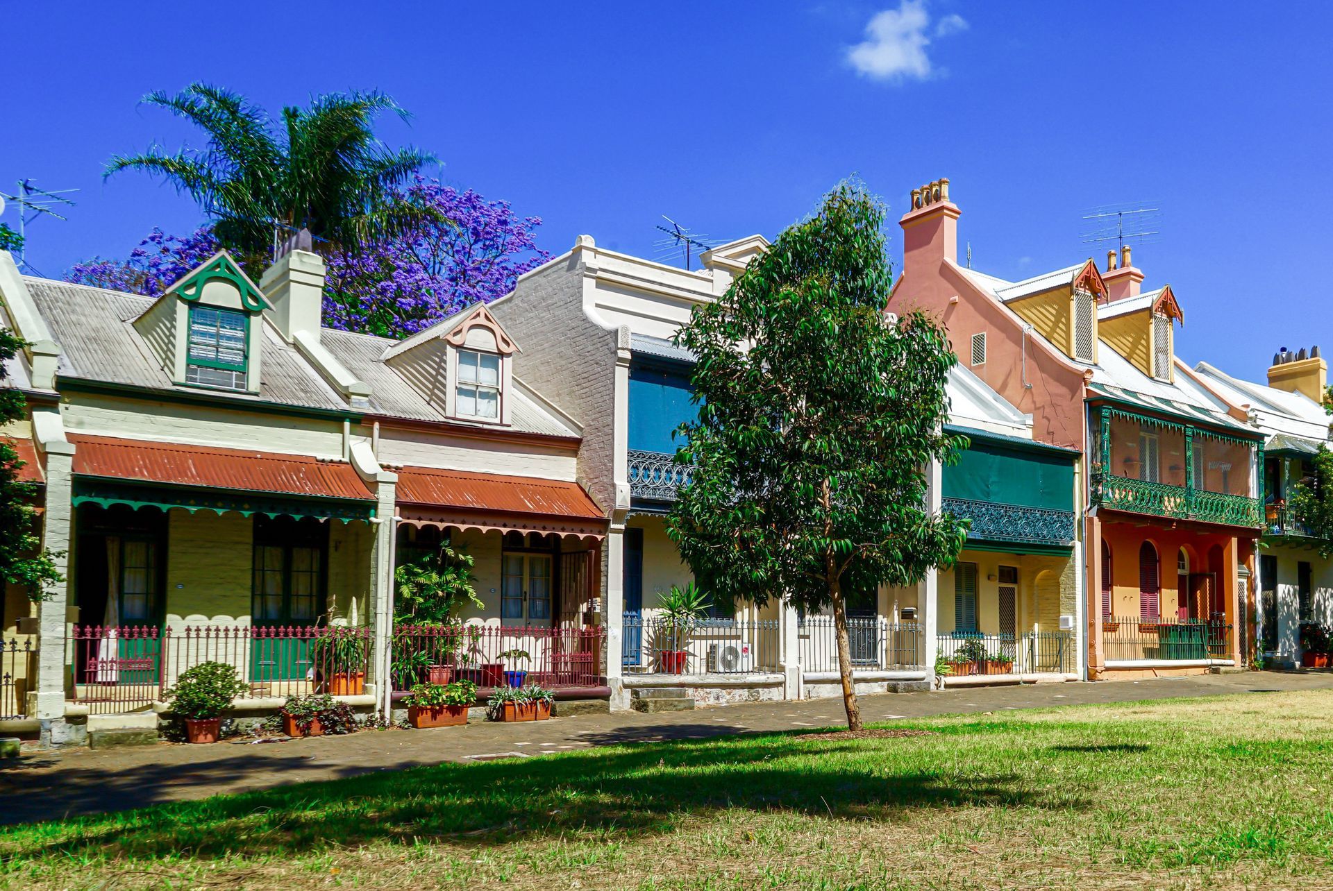 Colorful row of historic storefronts with porches, a tree, and a bright blue sky on a sunny day