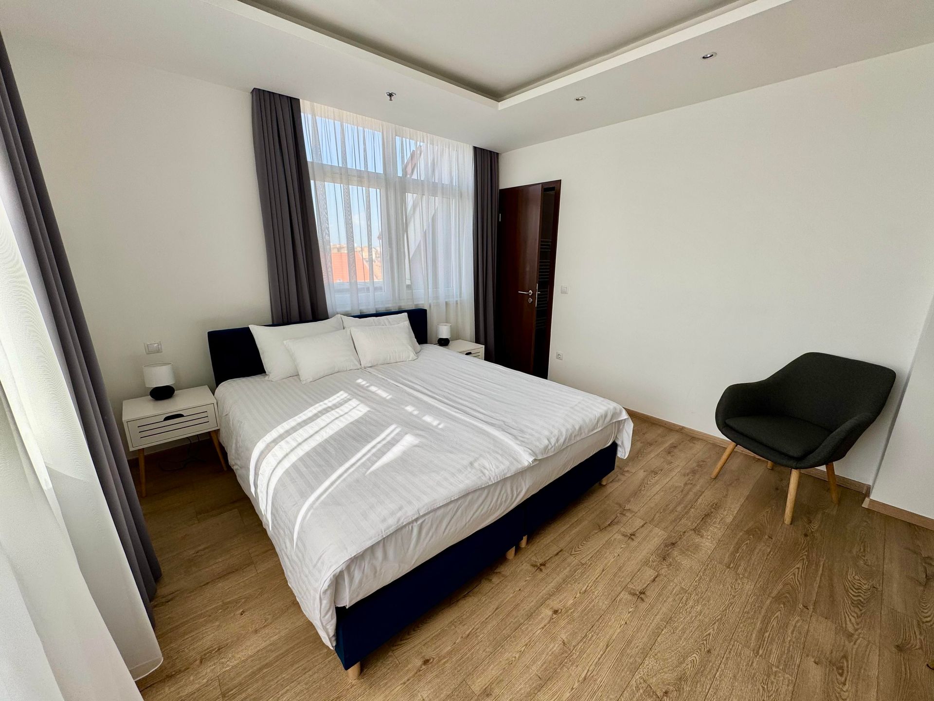 Bedroom with a bed, chair, nightstands, and window with natural light.