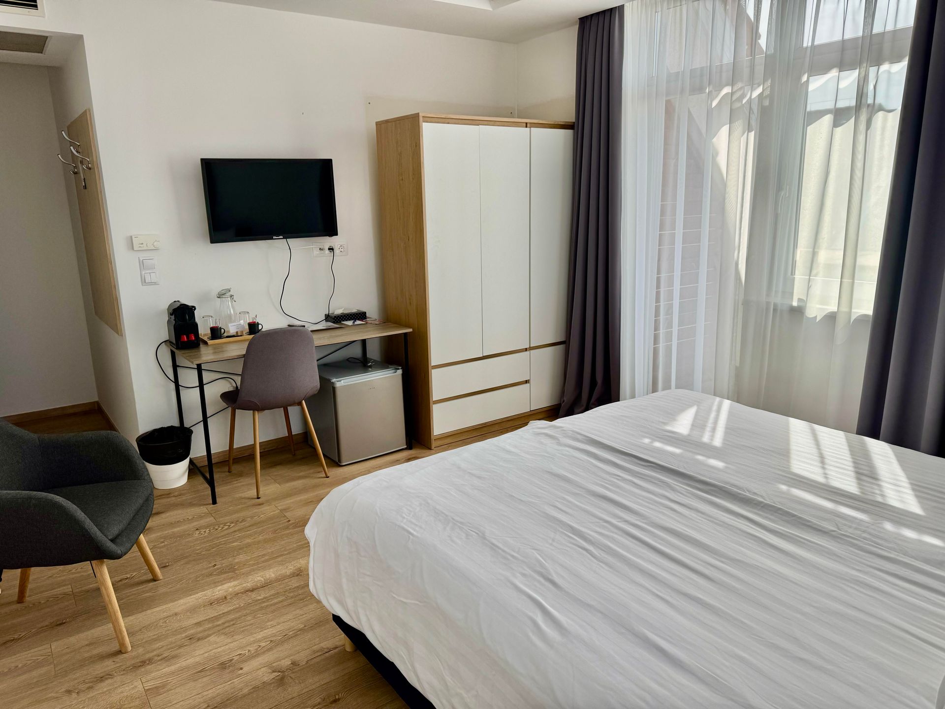 Hotel room with a bed, wardrobe, desk, TV, and window with curtains.