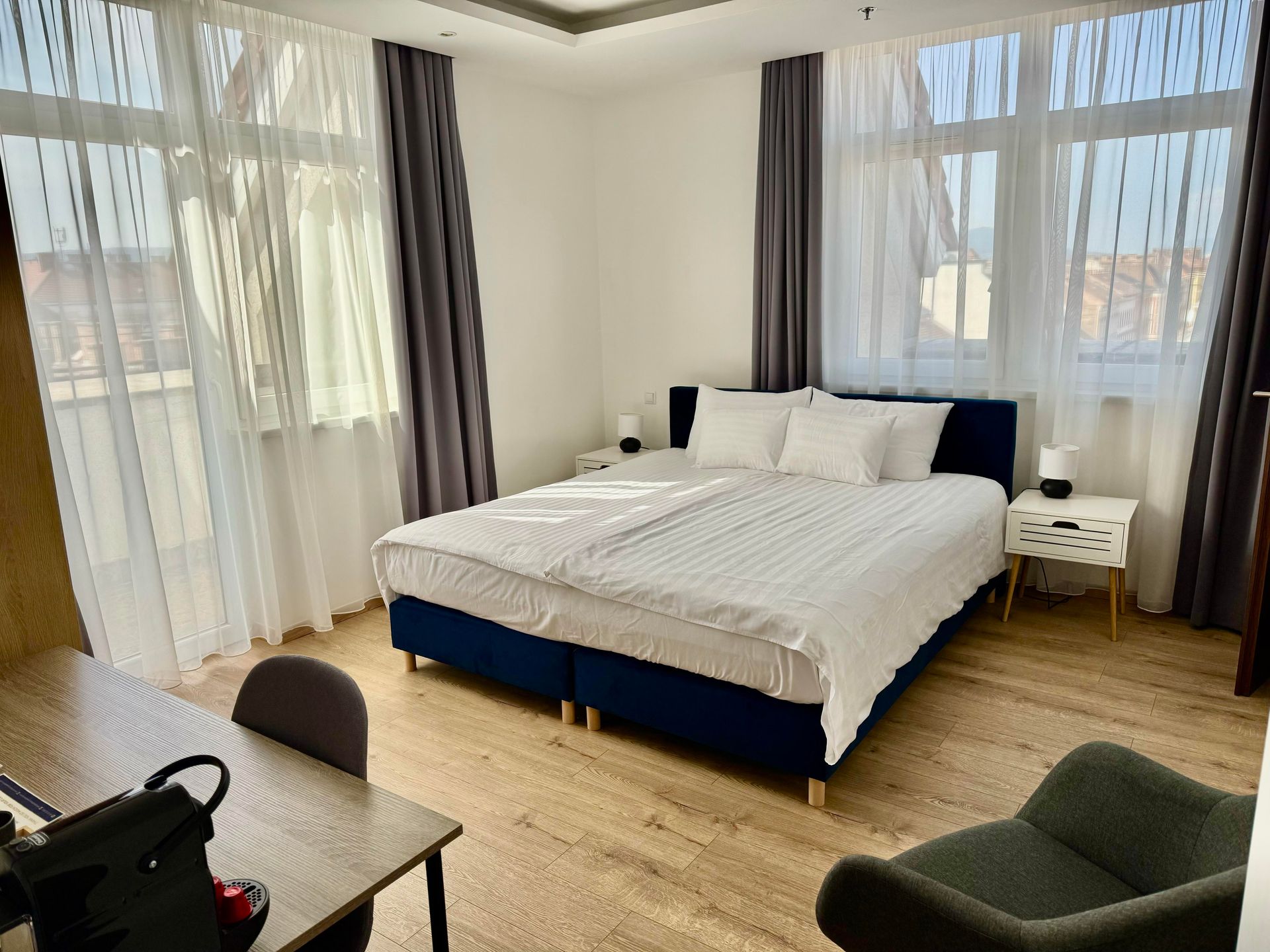 Bedroom with a double bed, dark blue headboard, white linens, two windows, and a desk.