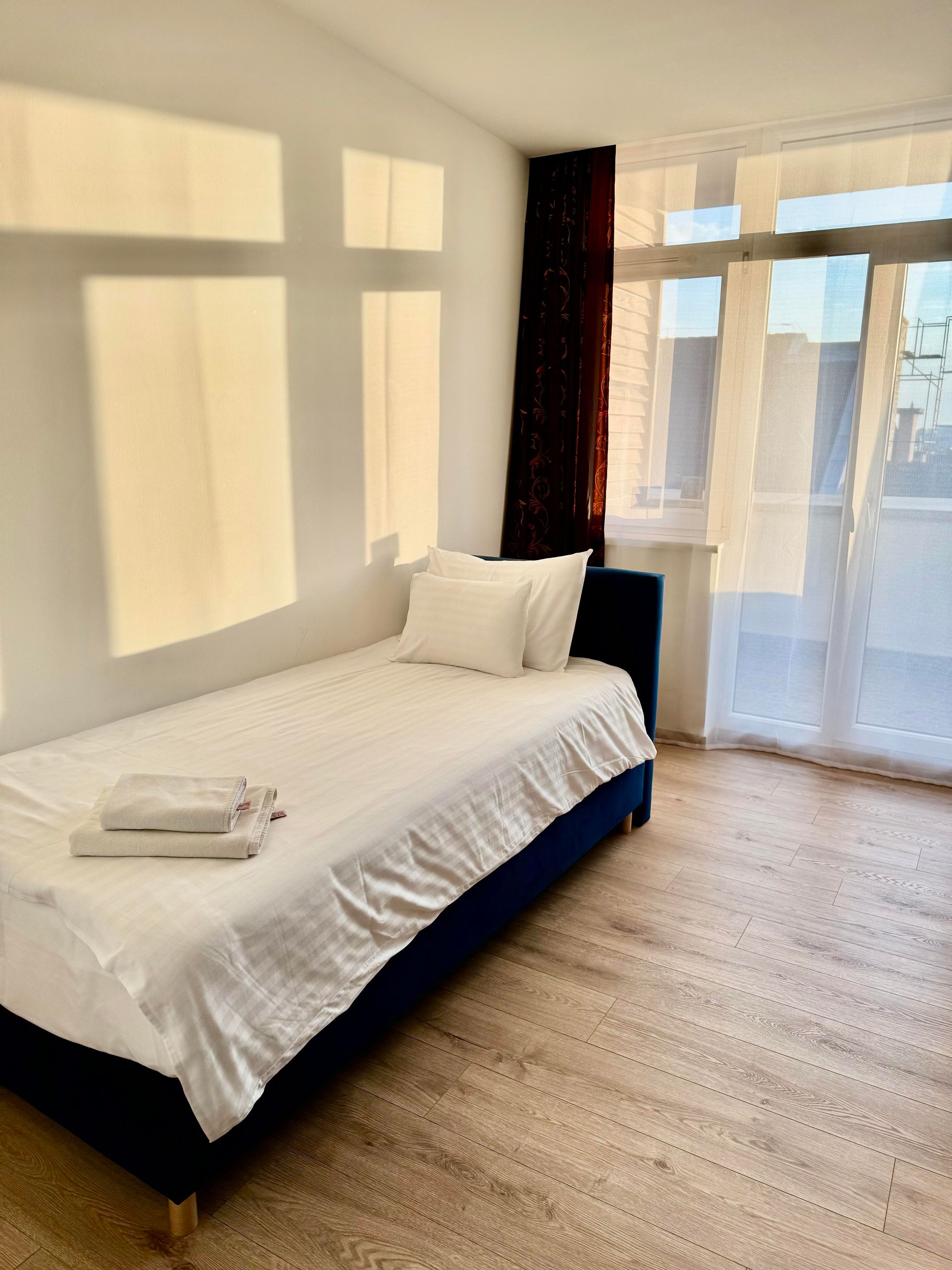 A bedroom with a single bed and light streaming through windows.