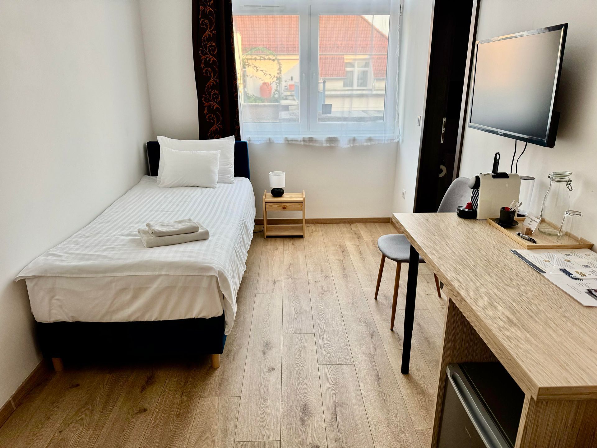 Hotel room with a twin bed, desk, small nightstand, and window.