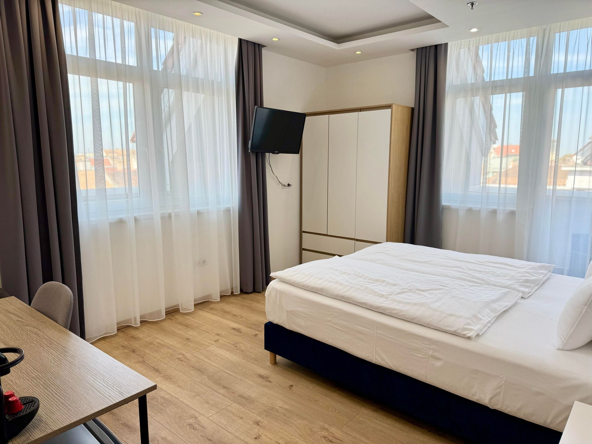 Bedroom with bed, wardrobe, TV, desk, and windows with curtains.