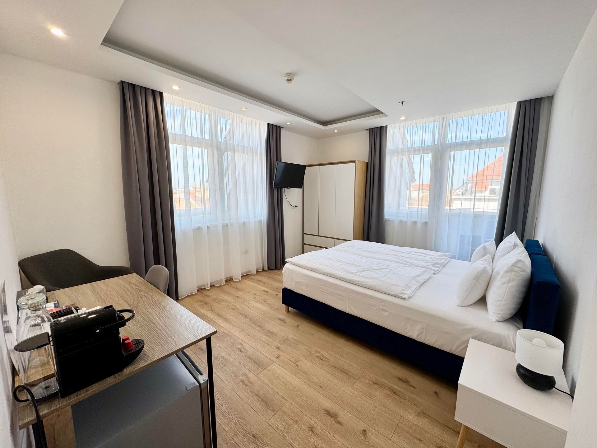 Bedroom with a bed, desk, wardrobe, and windows with curtains.
