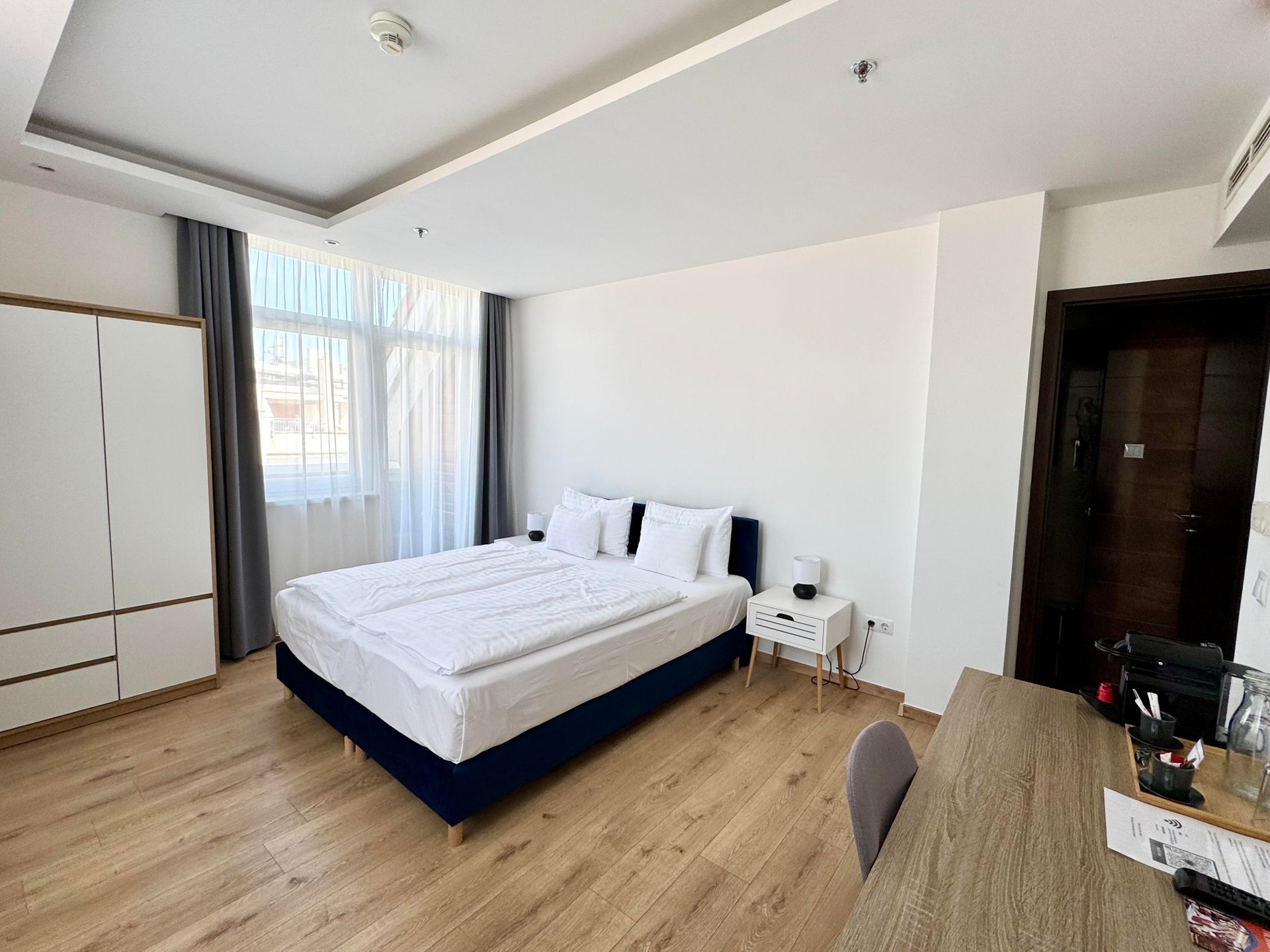 Bedroom with a double bed, wardrobe, desk, and a window with sheer curtains.