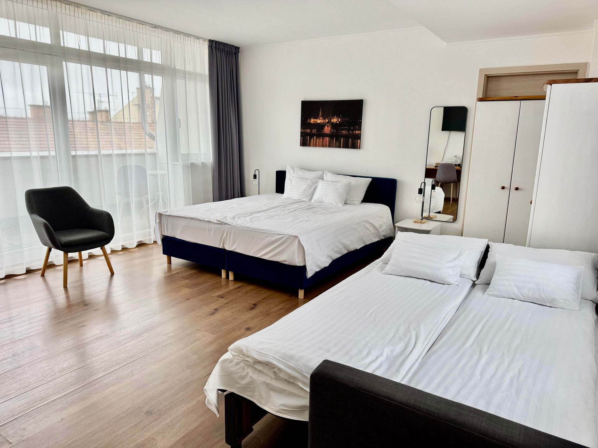 Bedroom with three beds, a chair, and a large window with a cityscape view.