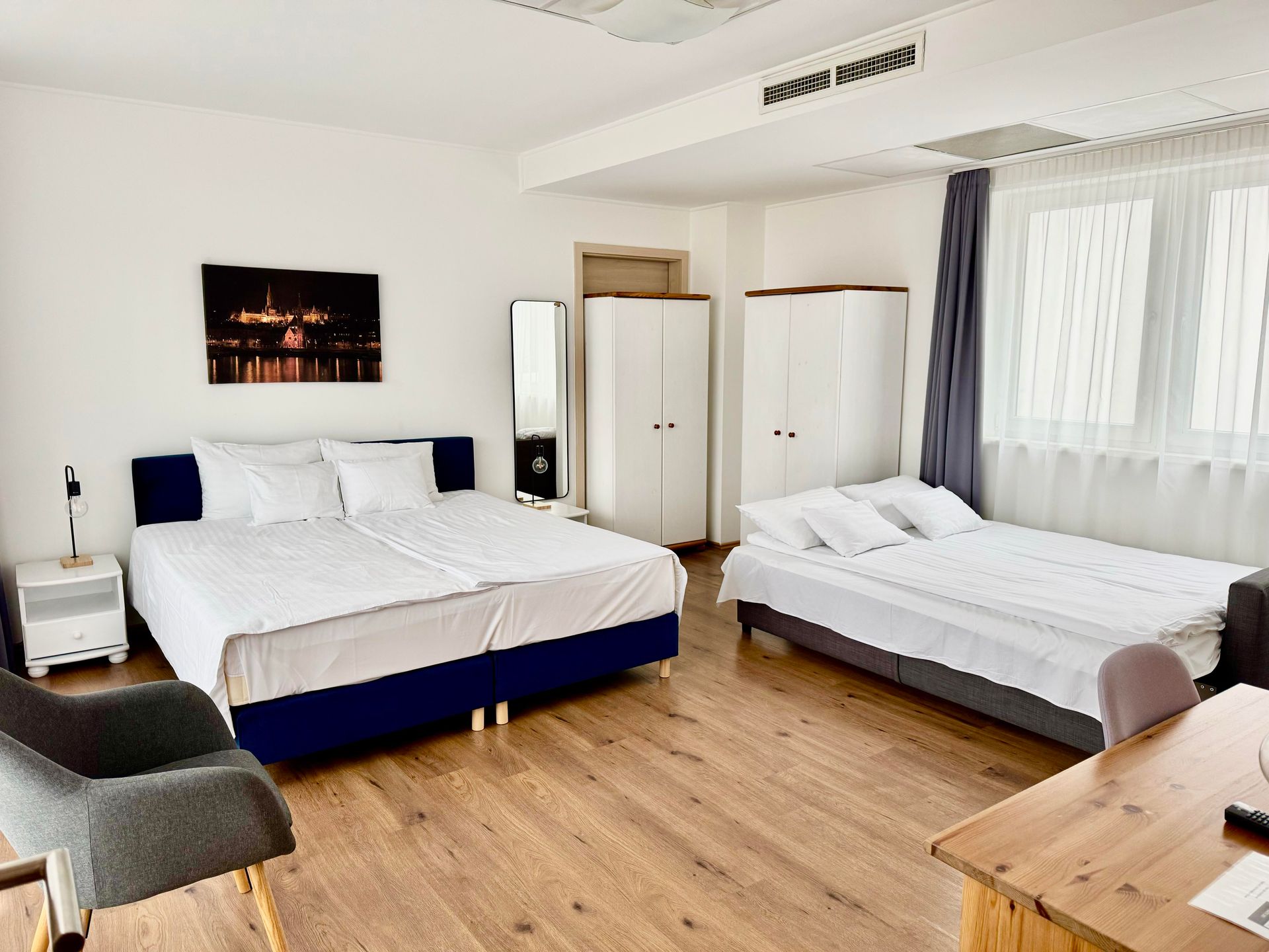 Bedroom with two beds, white bedding, wooden floors, two white wardrobes, and a window.