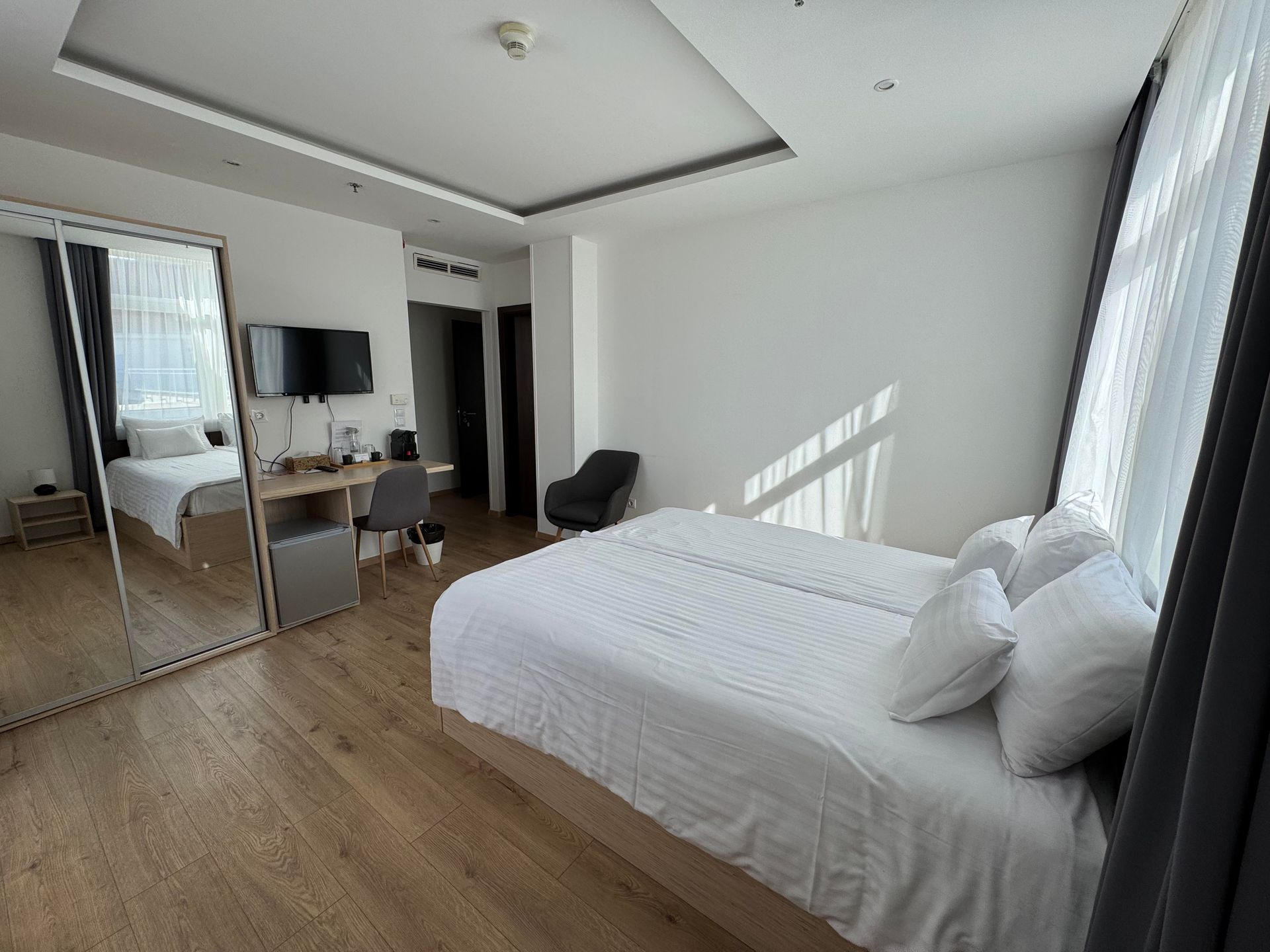 Hotel room with two beds, large mirror, desk, and chair. Bright, natural lighting.