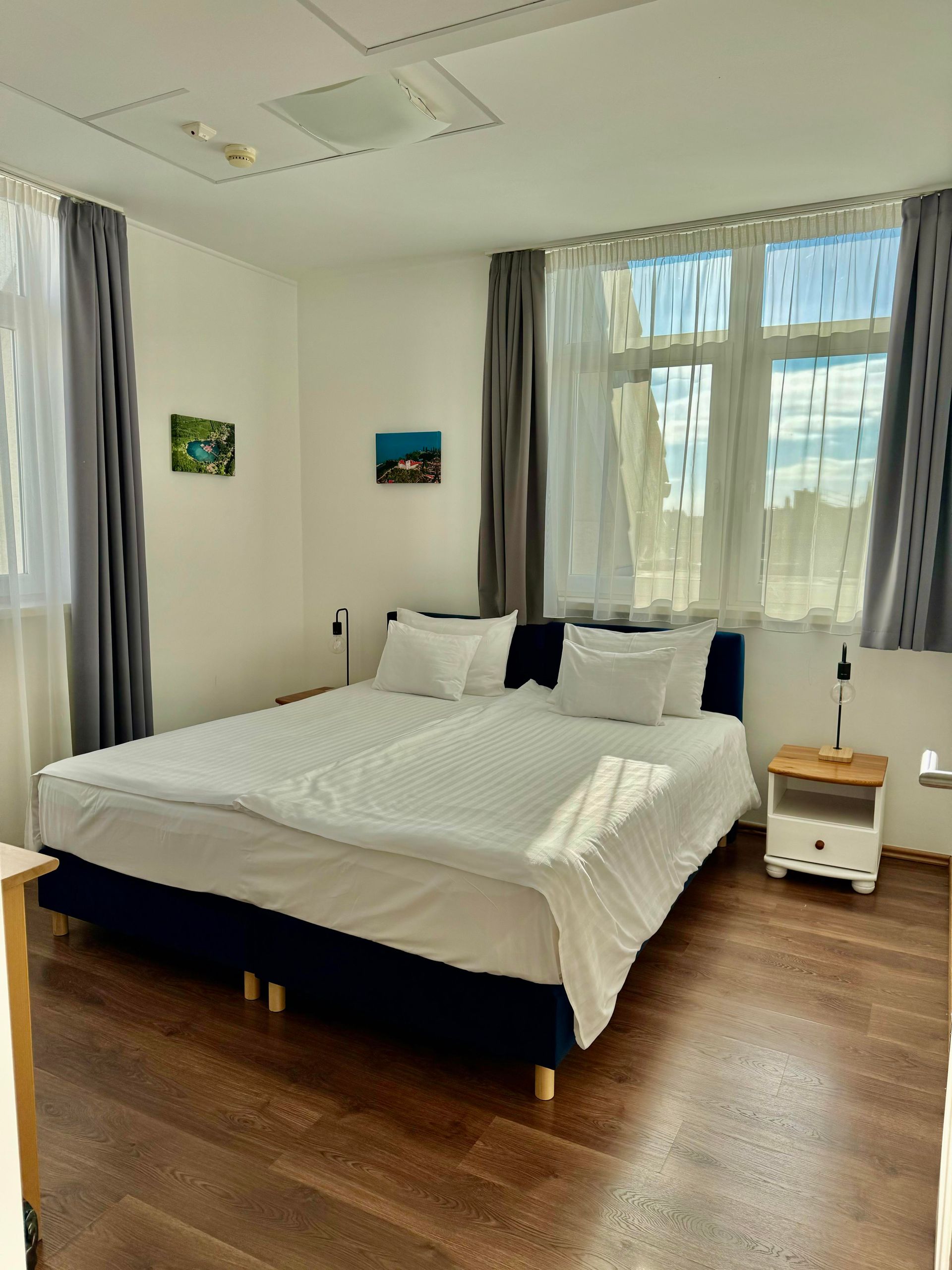 Bedroom with large bed, white bedding, blue headboard, wooden floor, and a window.