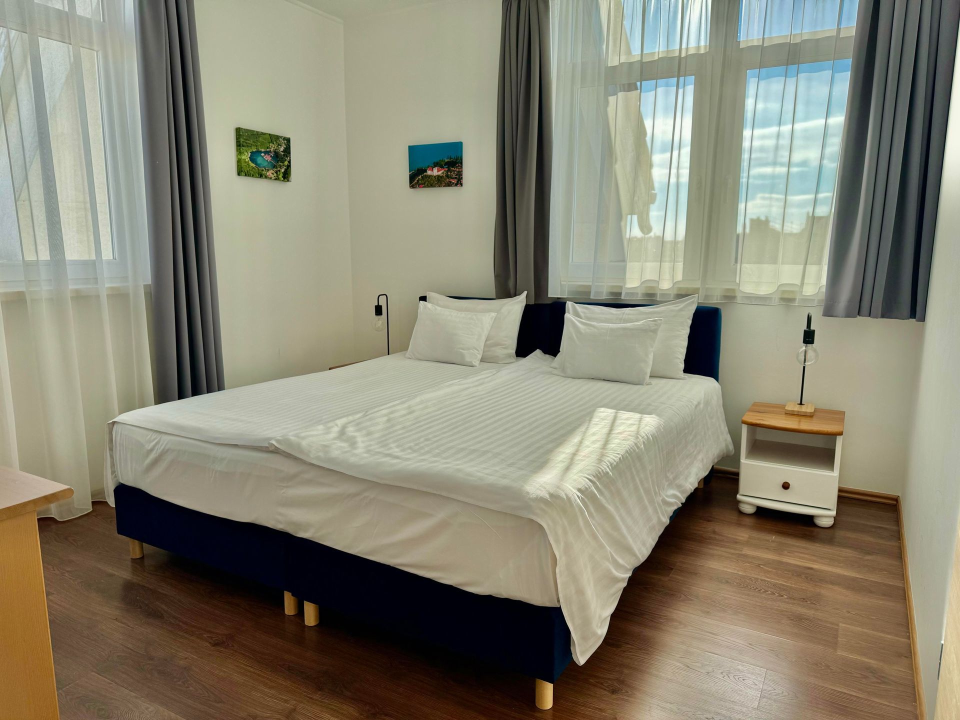 Bedroom with a blue bed, white bedding, nightstand, and two small paintings on the wall.
