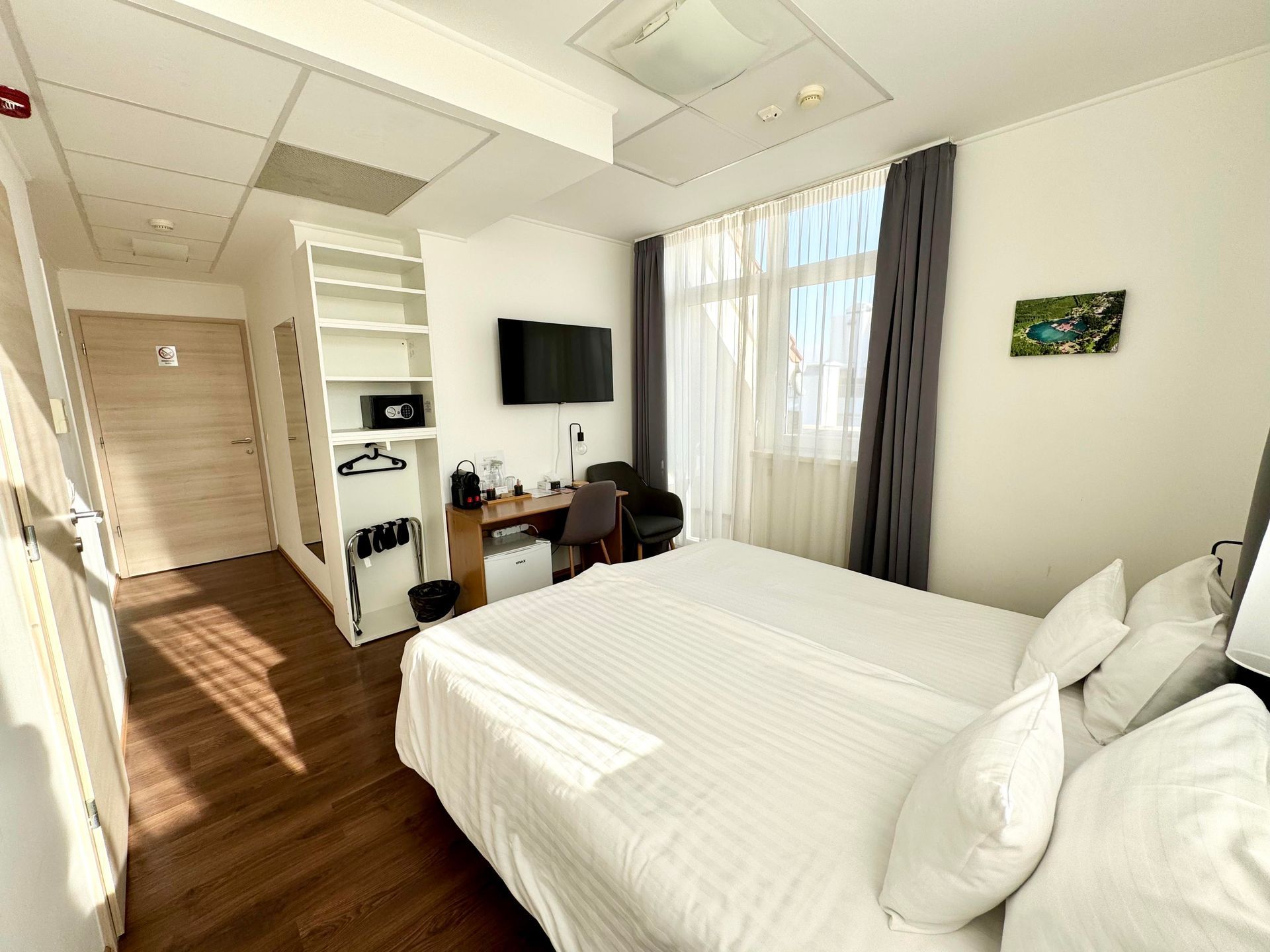 Hotel room with two beds, desk, TV, closet, and a window with curtains.