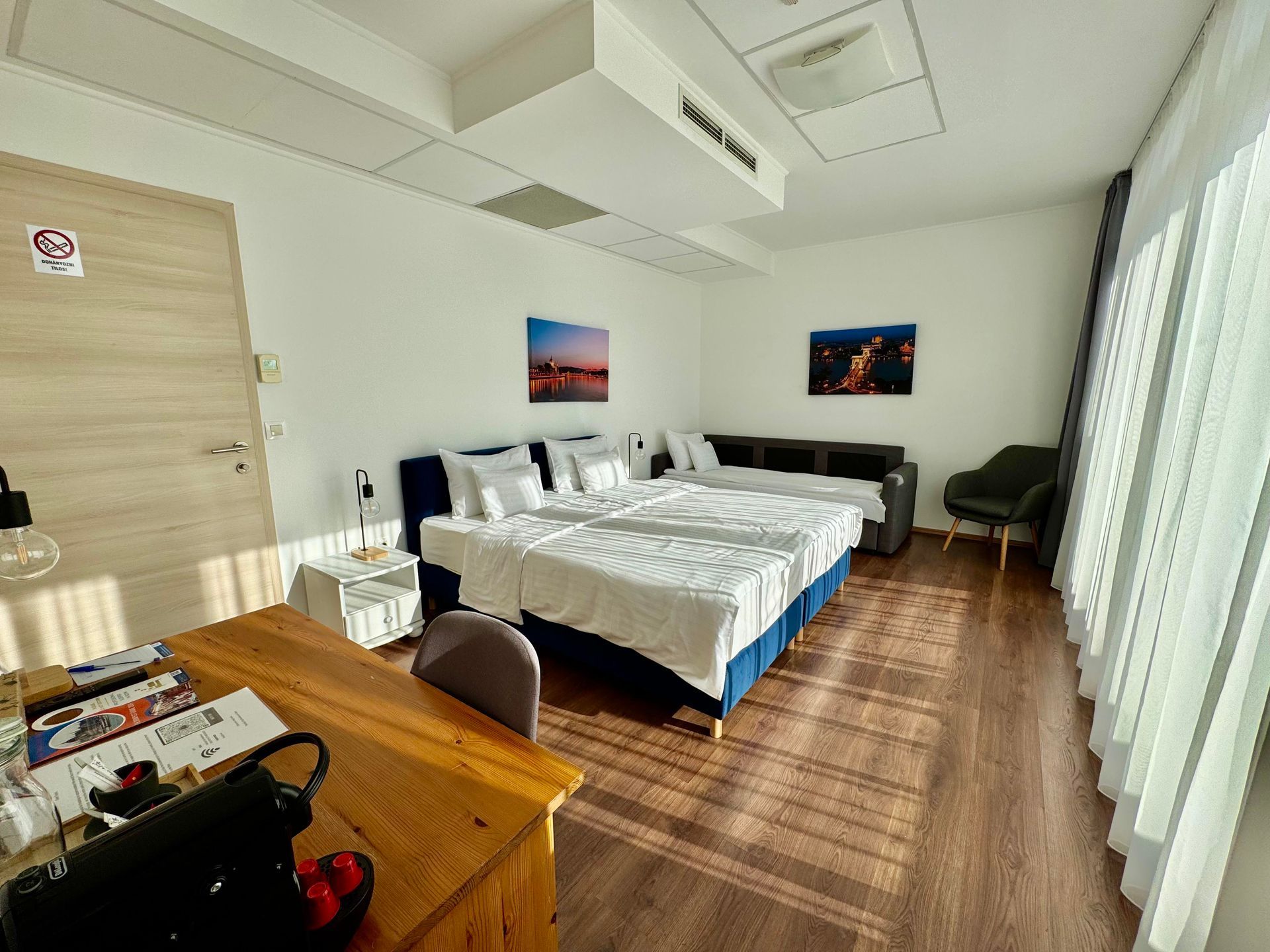 Spacious hotel room with a large bed, seating area, desk, and sunlight streaming in.