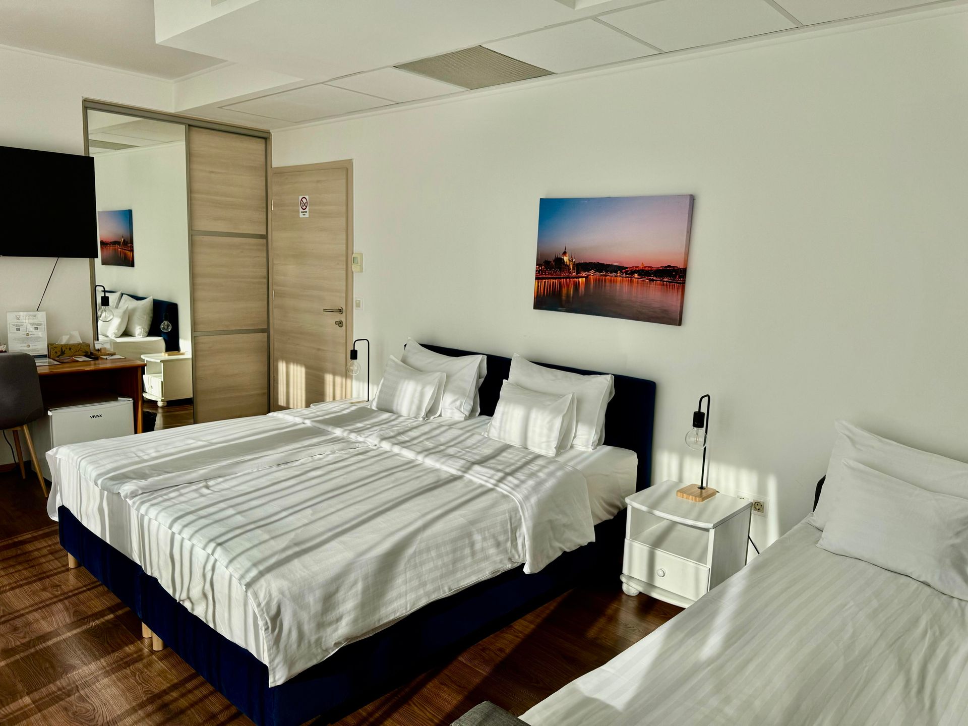 Hotel room with three beds, a mirror, and a sunset print.