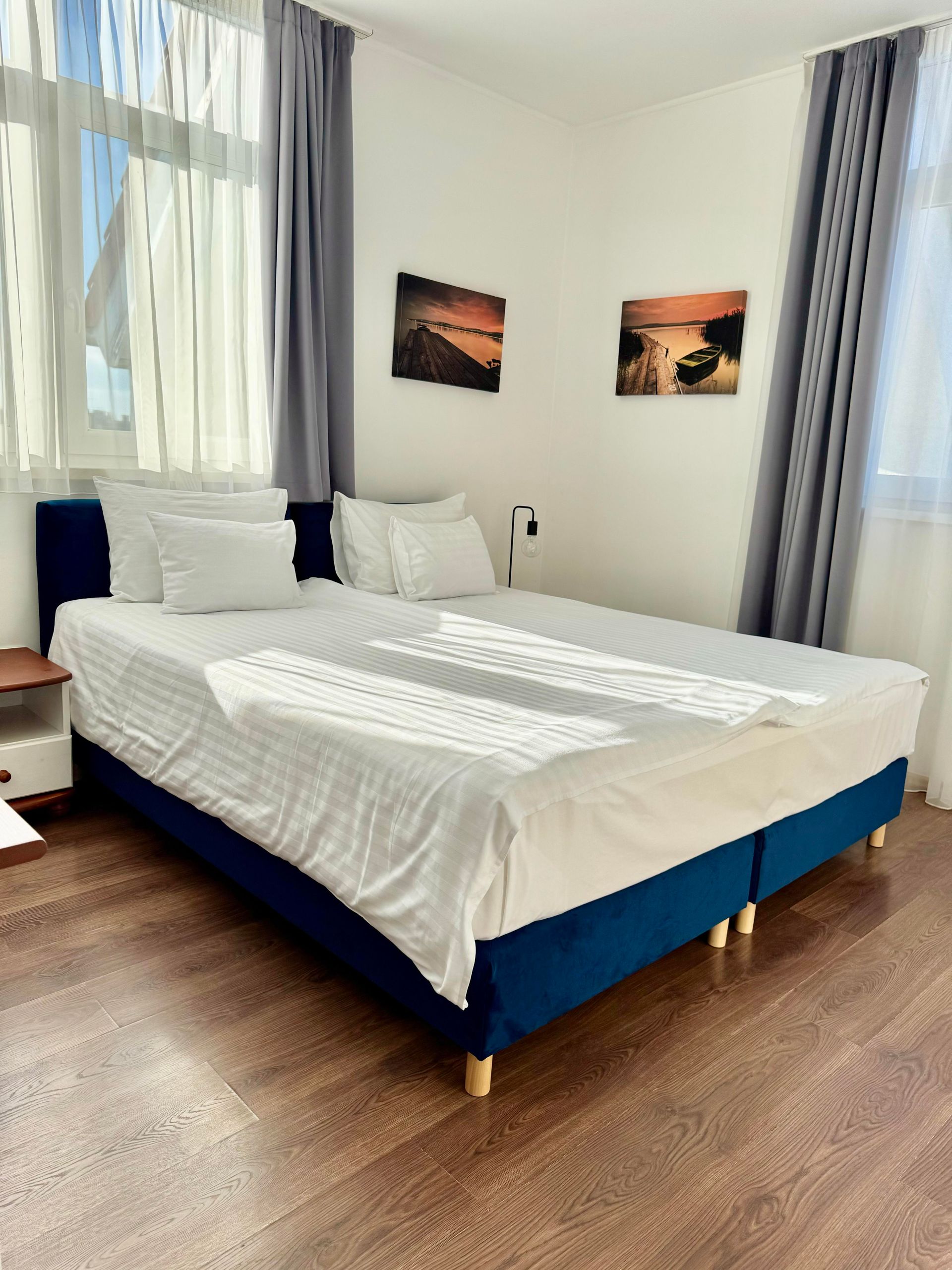 Bedroom with a blue bed, white bedding, and two landscape paintings on the wall.