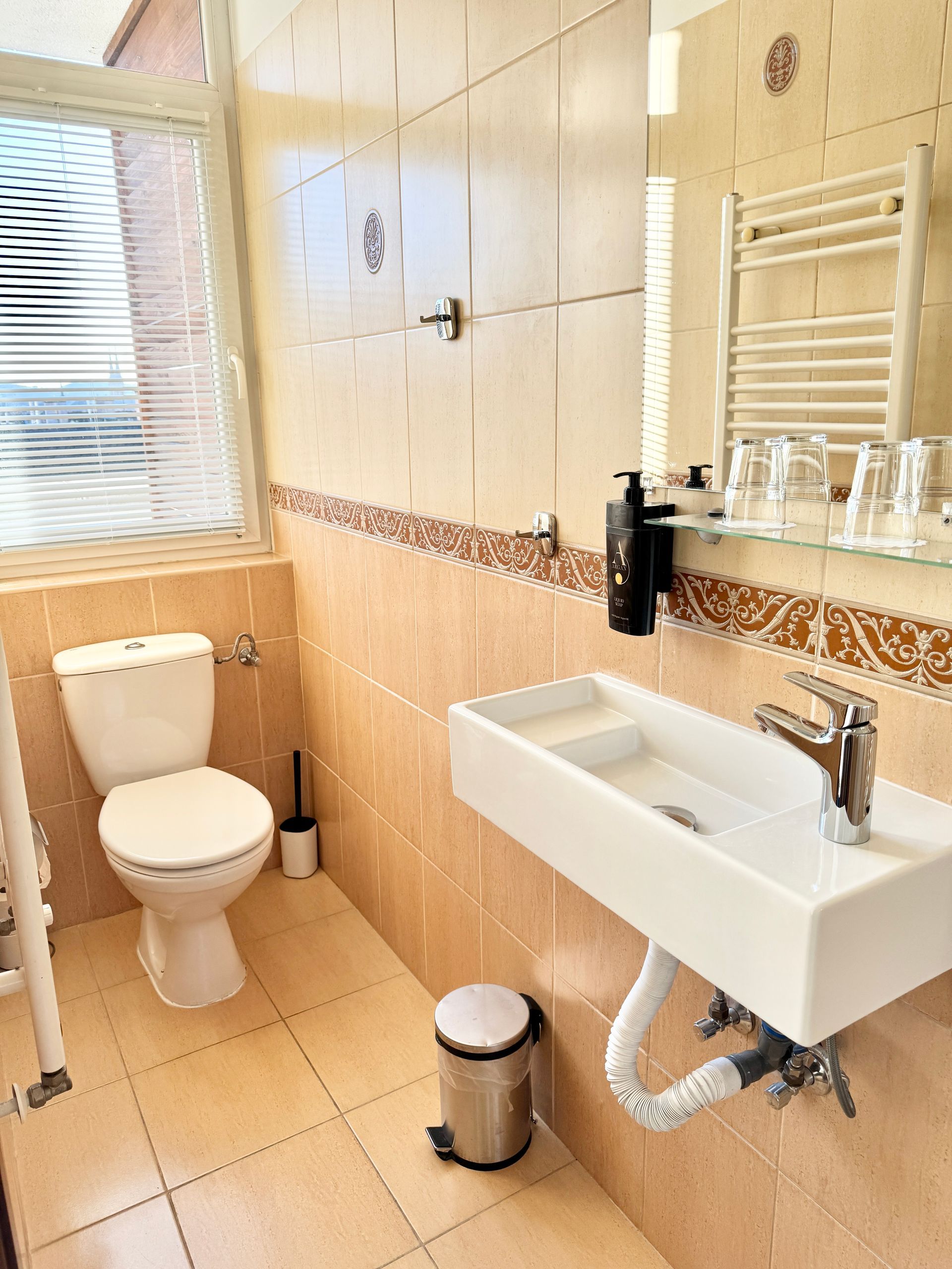 Small bathroom with a toilet, sink, mirror, and towel rack. Beige tile walls and floor.