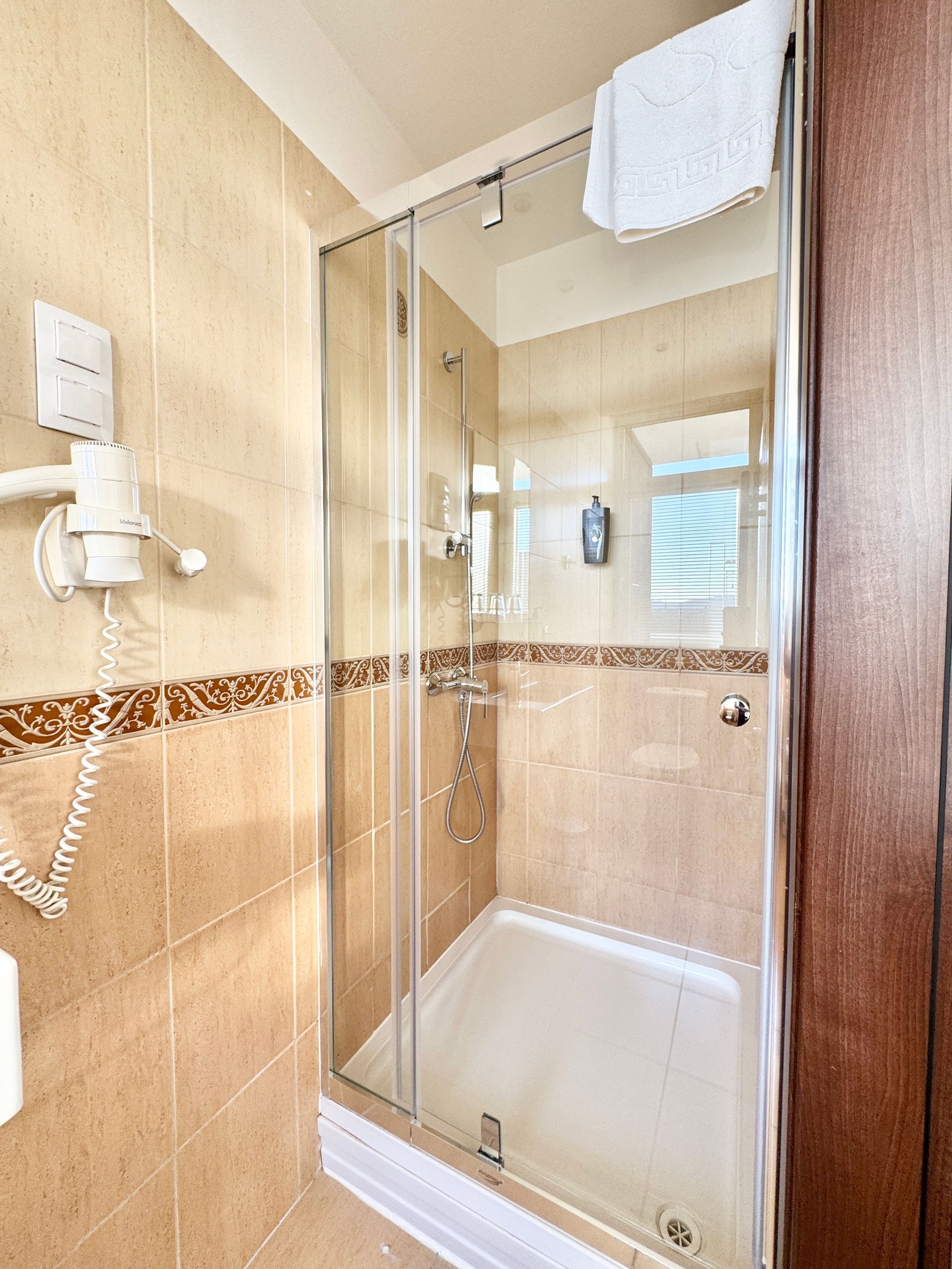 Shower with glass door in a bathroom with beige tile walls and a towel.