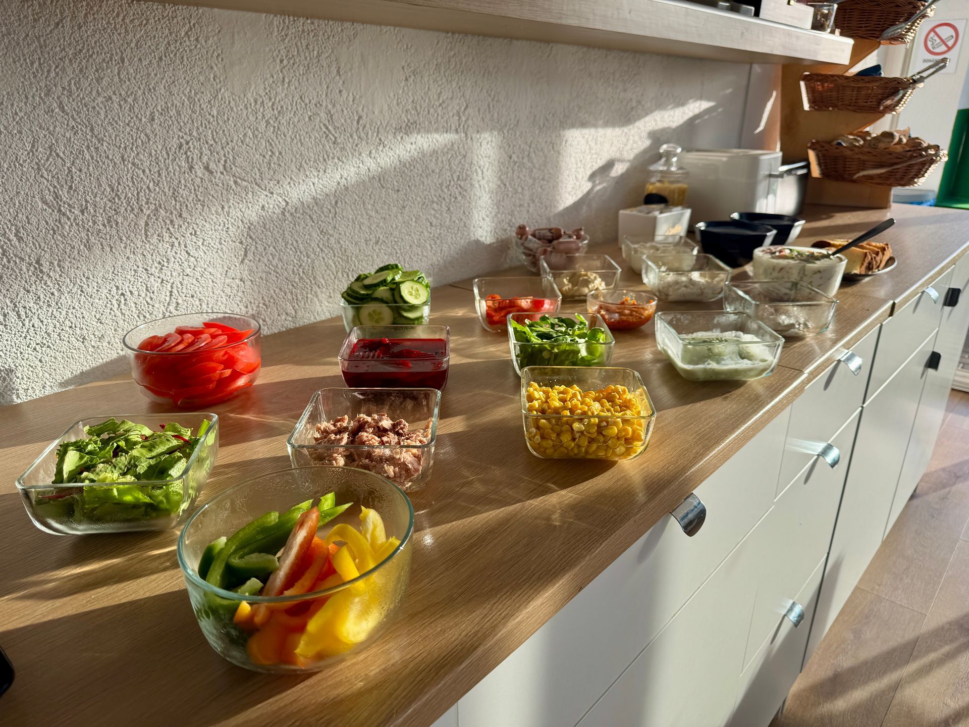 A buffet counter with glass bowls of various salad ingredients, including vegetables and tuna.