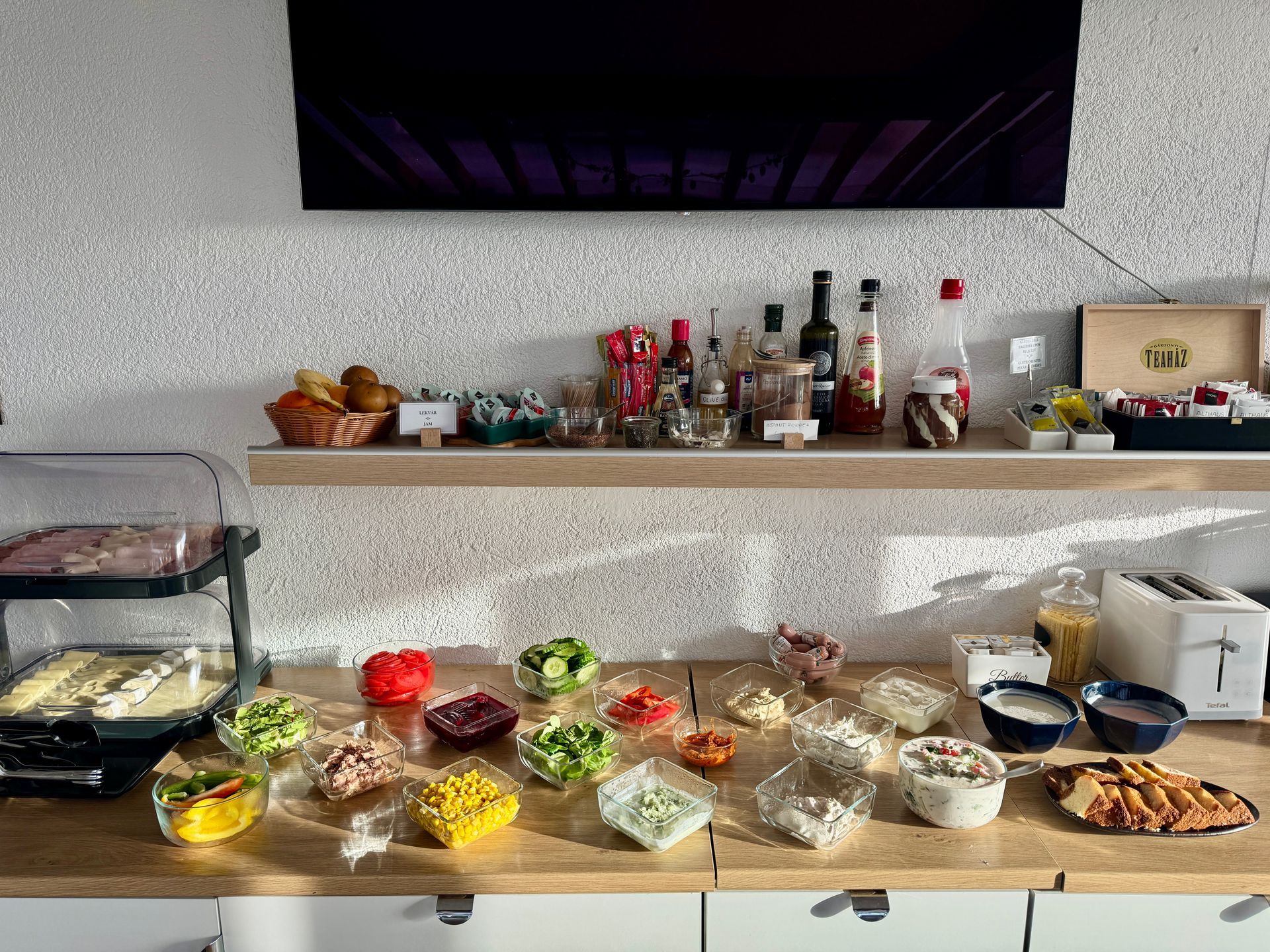 Buffet with various food items on a counter and shelf with a TV above.