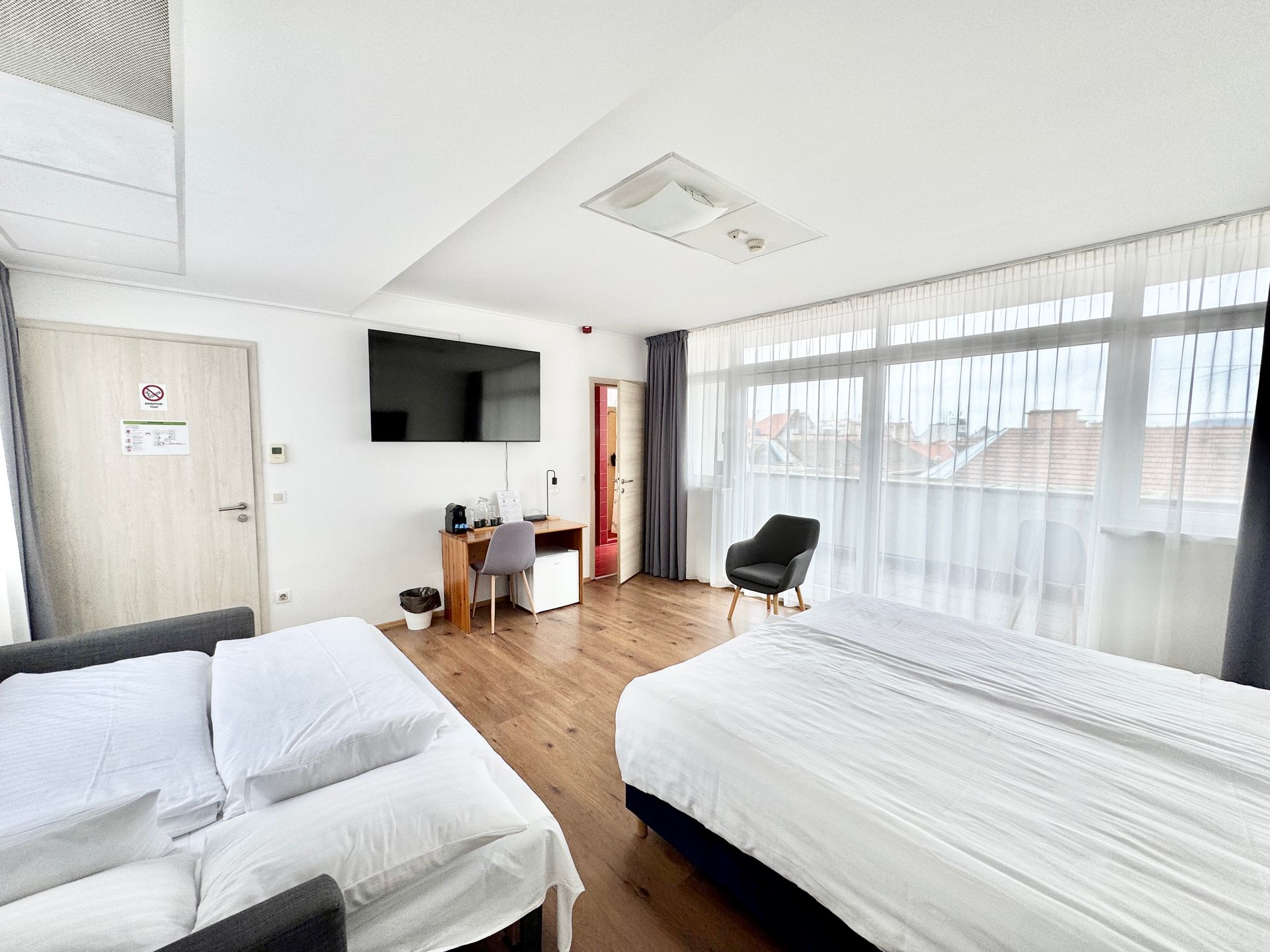 Hotel room with two beds, desk, TV, and large windows.