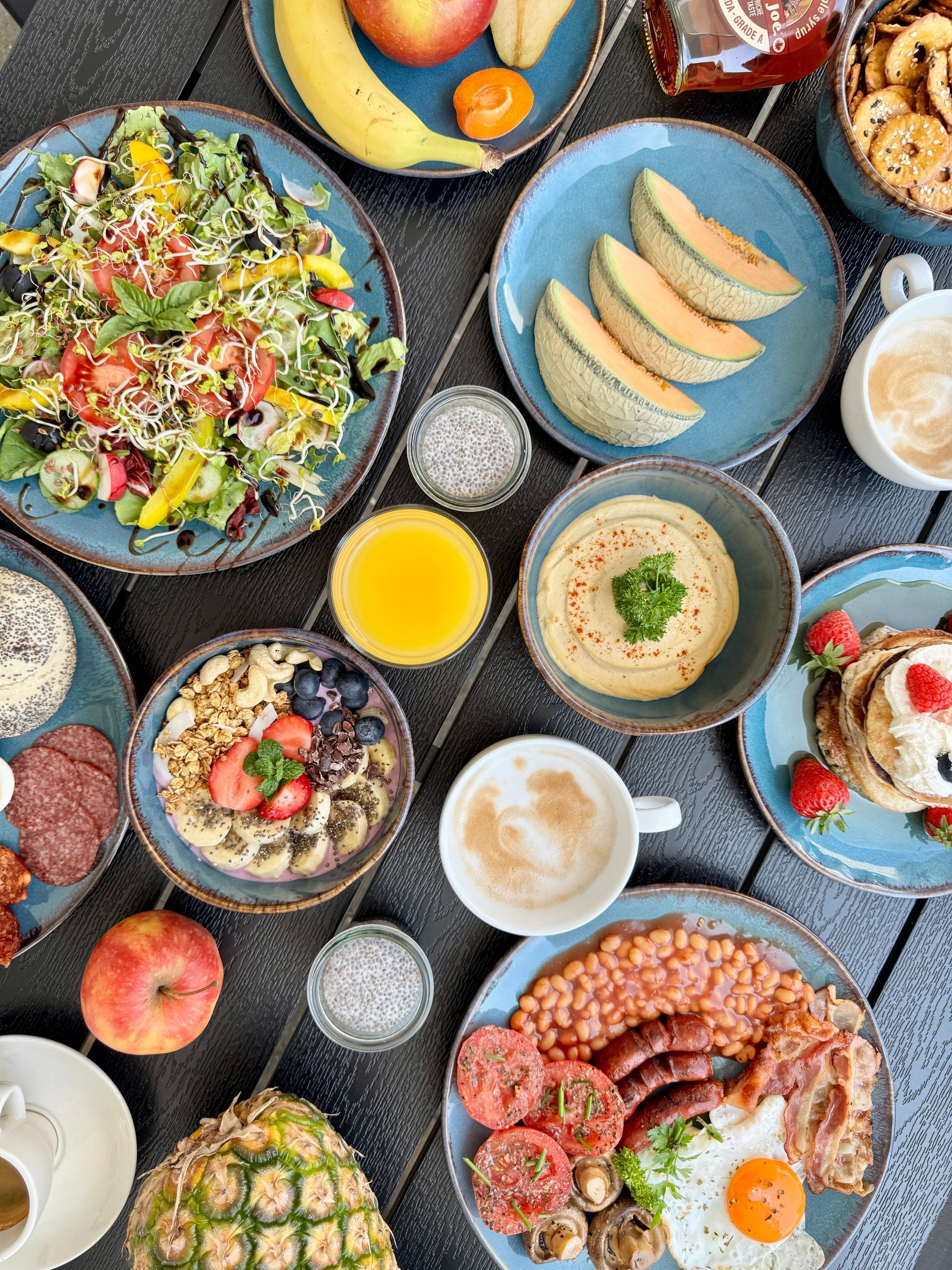 Overhead view of a breakfast spread with various dishes including fruits, salad, oatmeal, and a full English breakfast.