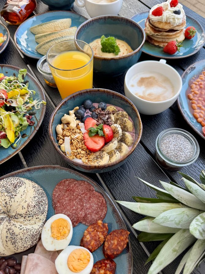 Overhead view of a breakfast spread on a dark wooden table with various dishes in turquoise bowls and plates.