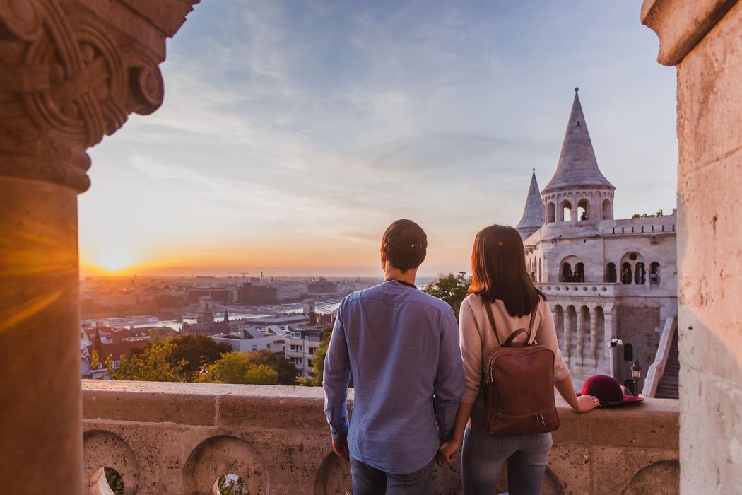 Couple overlooking Budapest cityscape at sunset, Fisherman's Bastion in view.