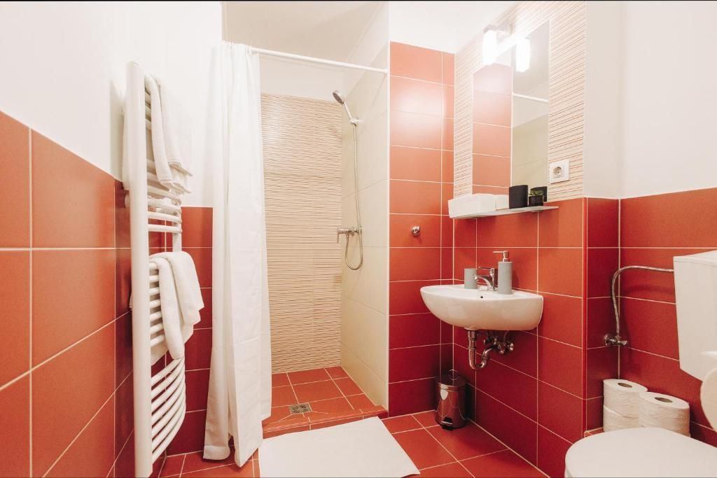 Red-tiled bathroom with a shower, sink, and toilet. White towels hang on a radiator.