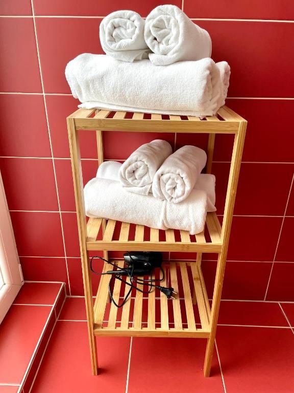 Wooden shelf with rolled white towels and a hairdryer, in a bathroom with red tiles.