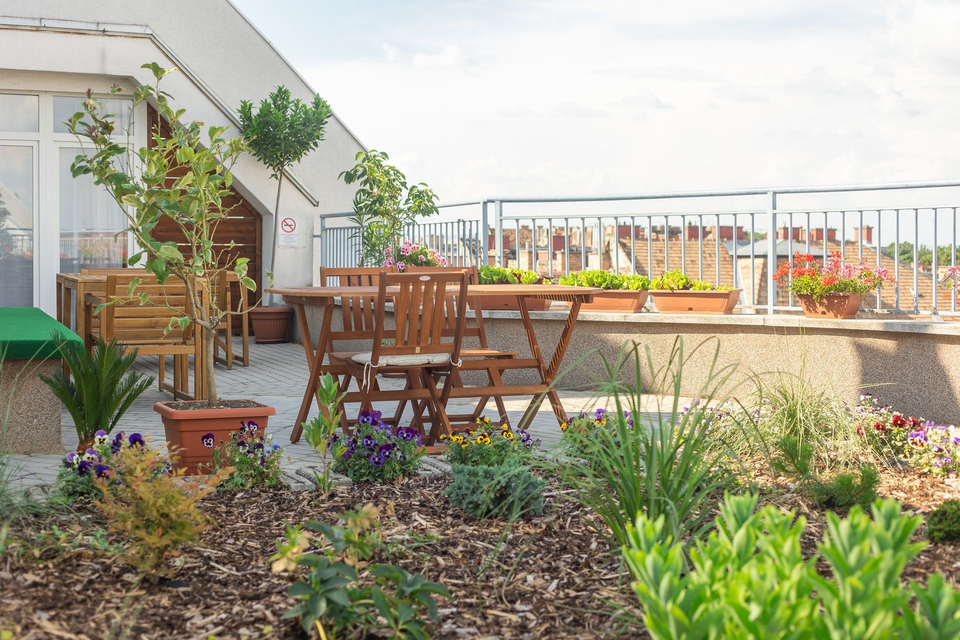 Rooftop patio with wooden furniture, plants, and city view.