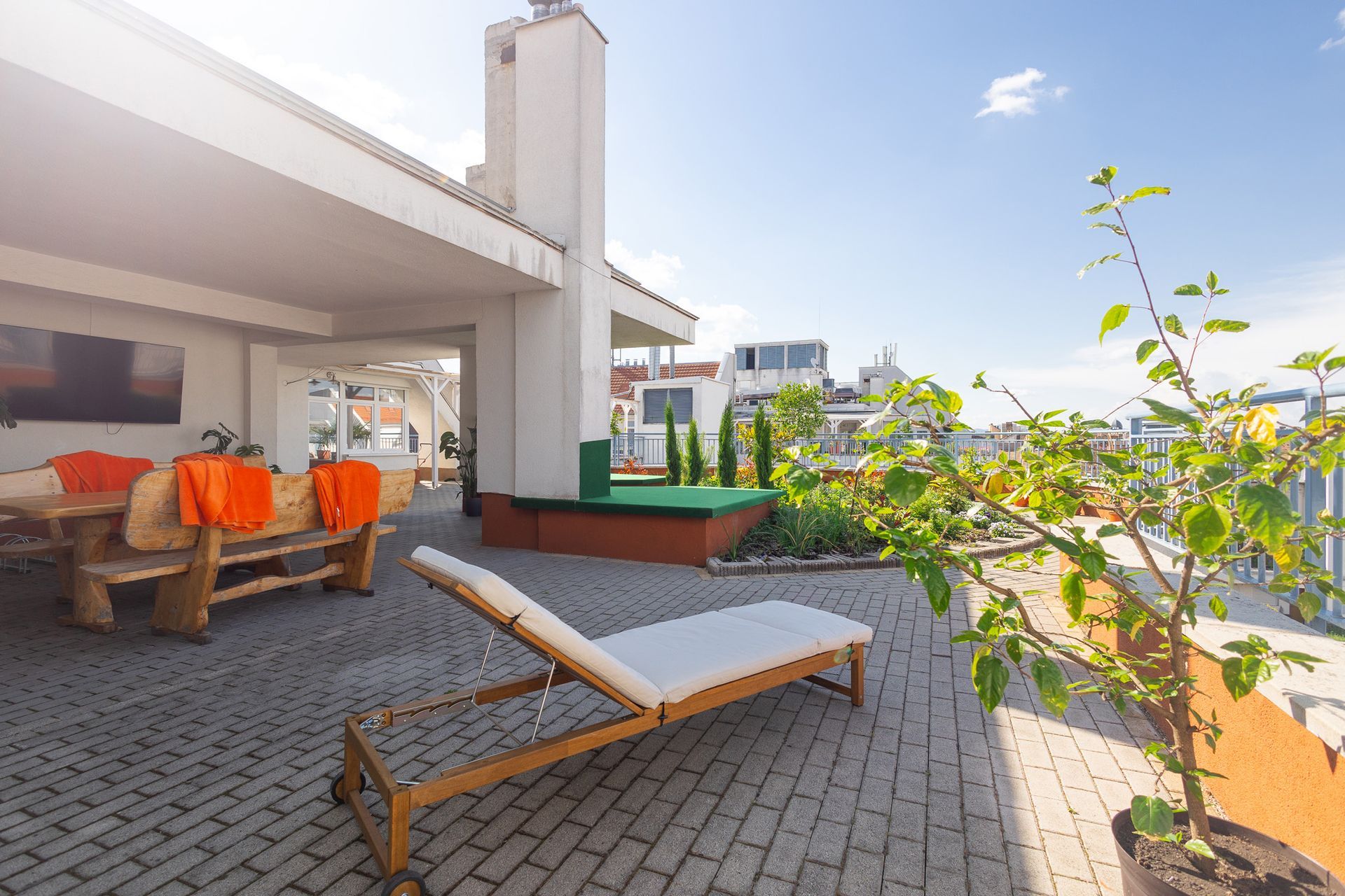 Rooftop patio with lounge chair, wooden table, and potted plant under a blue sky.