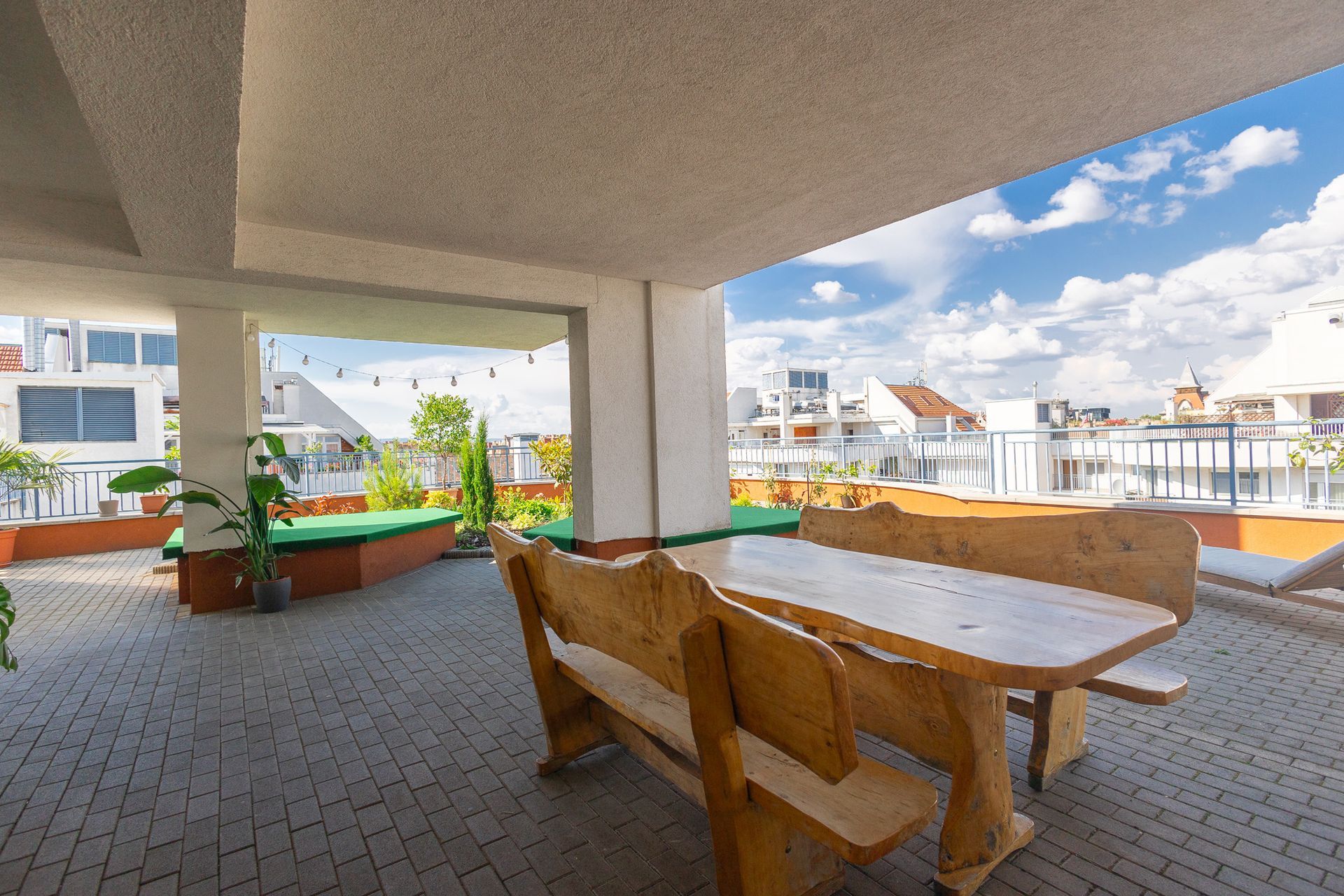 Patio with wooden table and benches, overlooking rooftops on a sunny day.