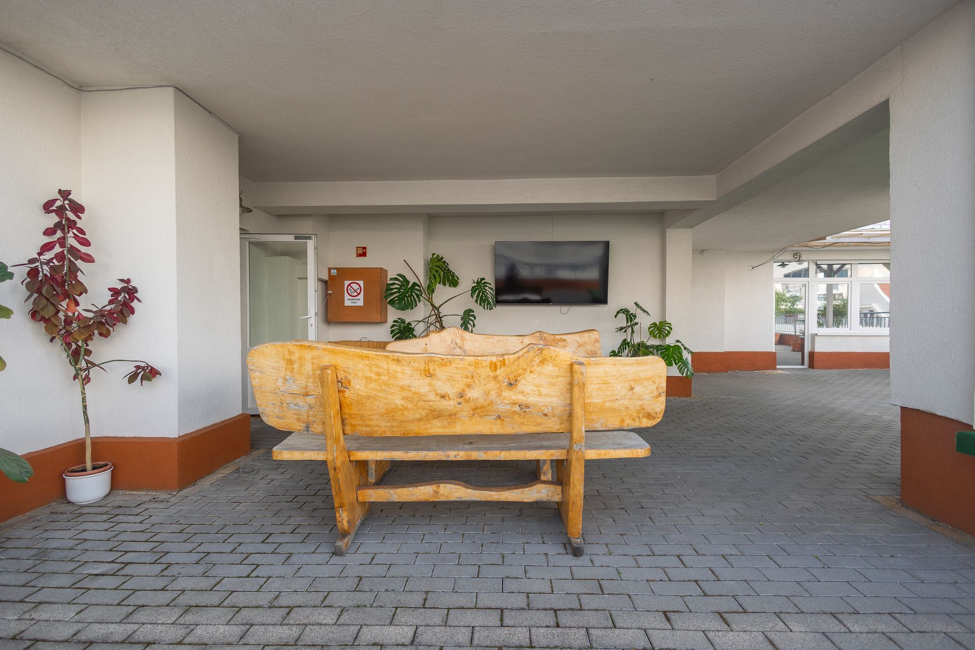 Covered patio area with a wooden bench, plants, and a wall-mounted TV.
