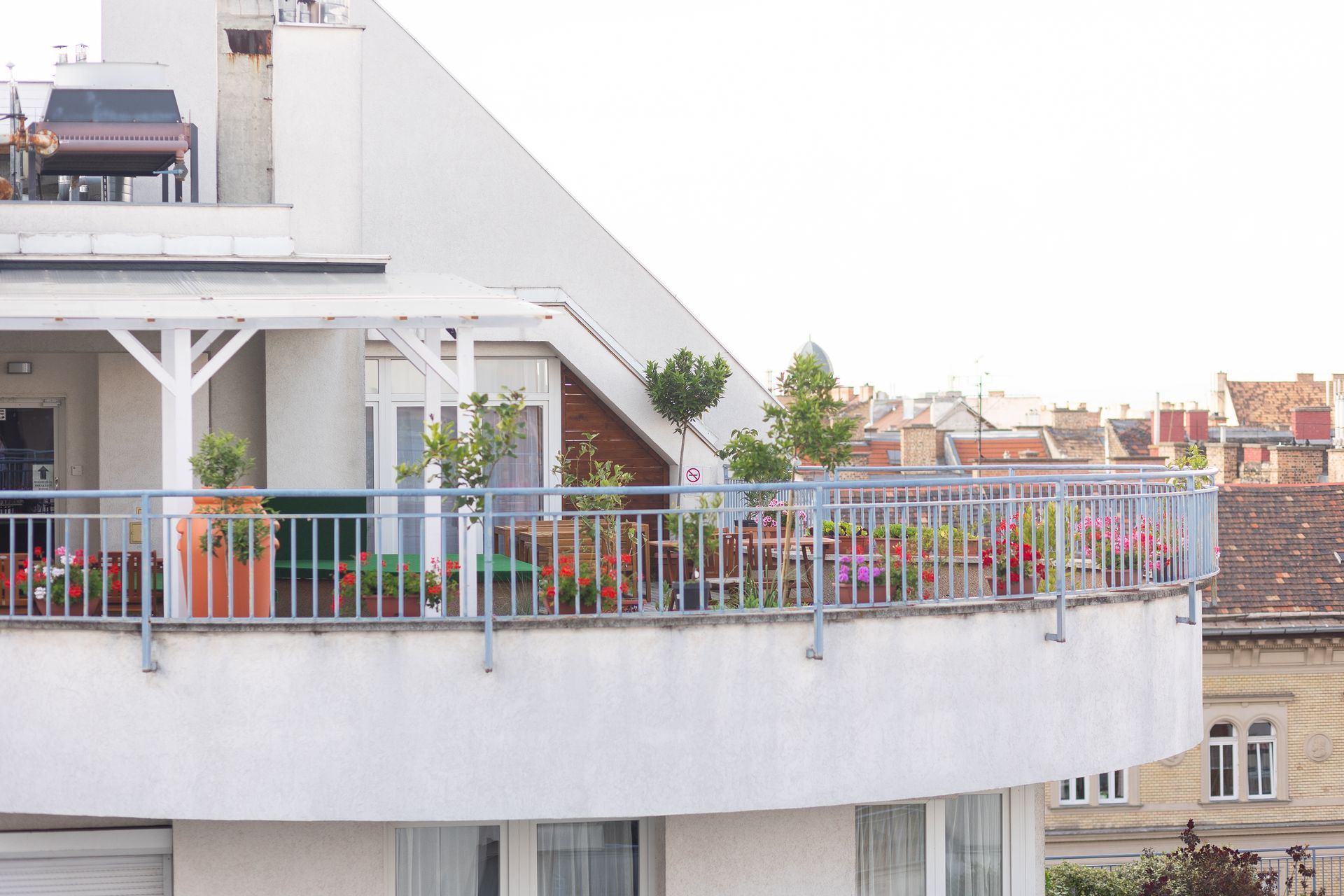 Curved balcony with potted plants and a metal railing, overlooking a city.