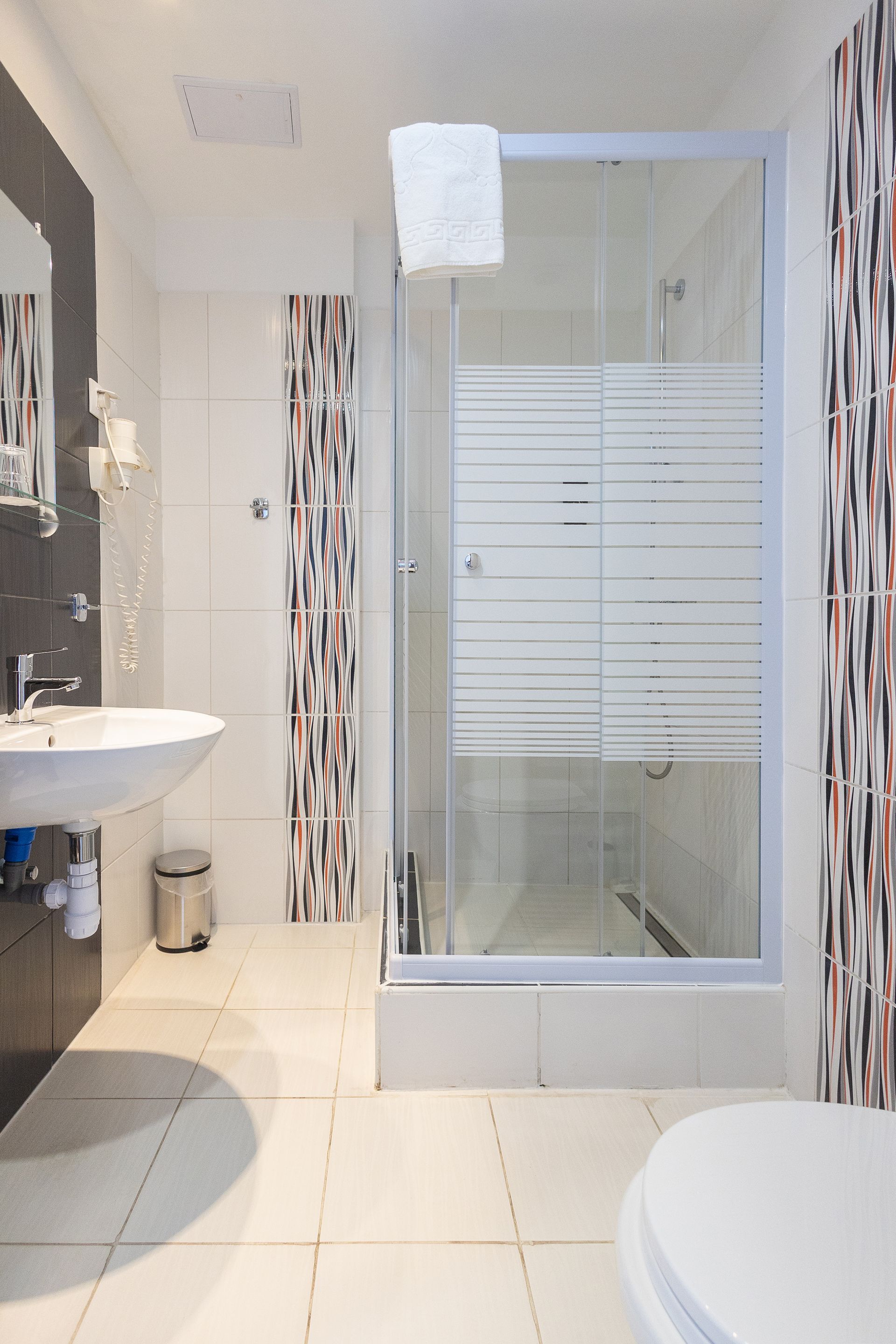 Modern bathroom with white and brown tiles, shower stall, toilet, and sink.