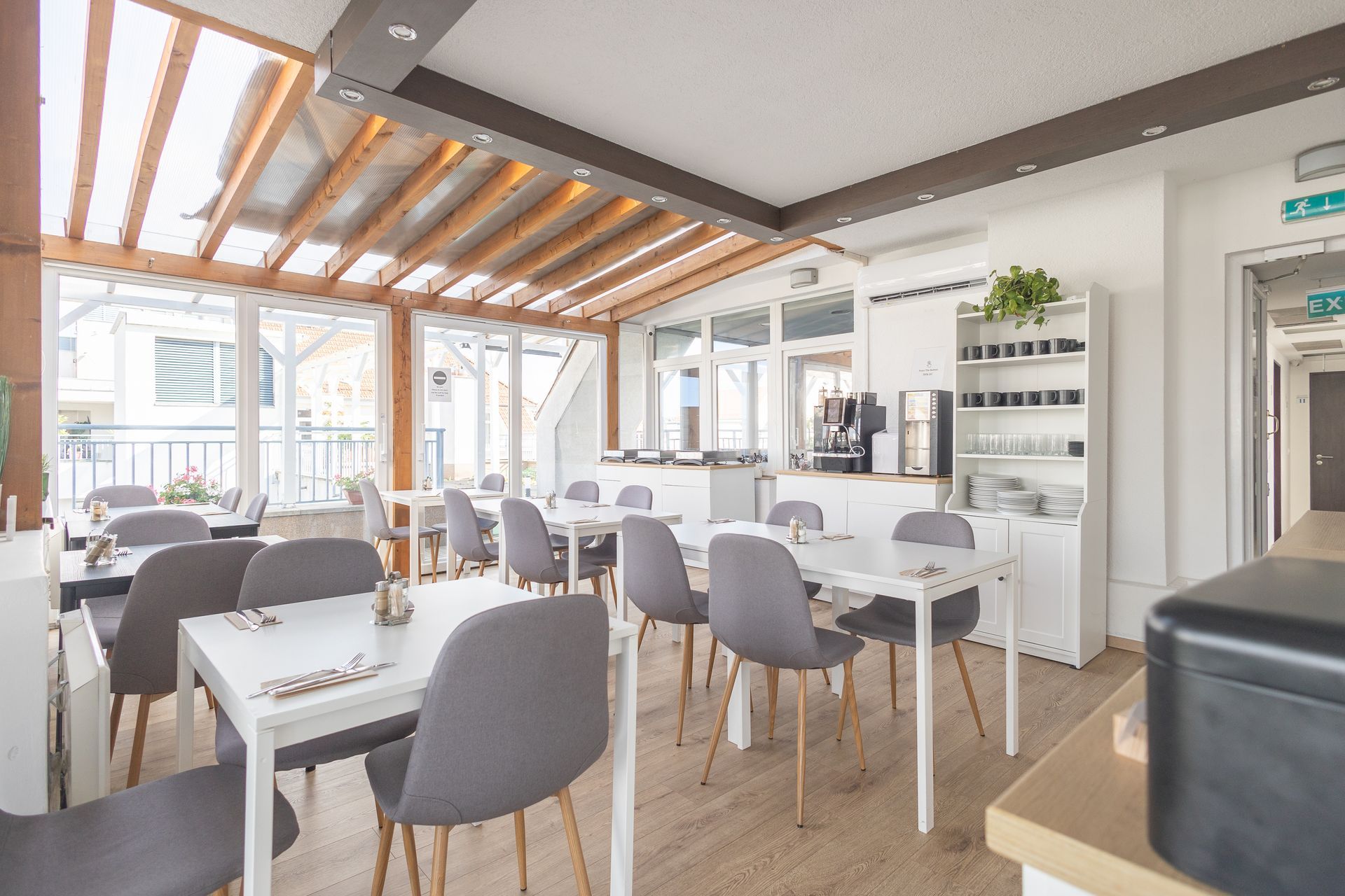 Bright dining room with white tables, gray chairs, and glass ceiling.